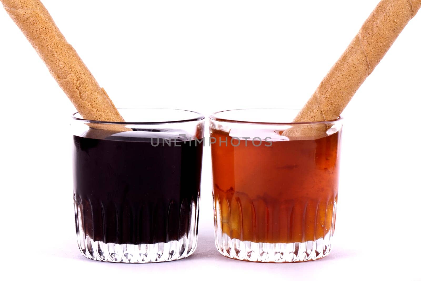 Close up view of a glass of honey and another of chocolate with cookie rolls.