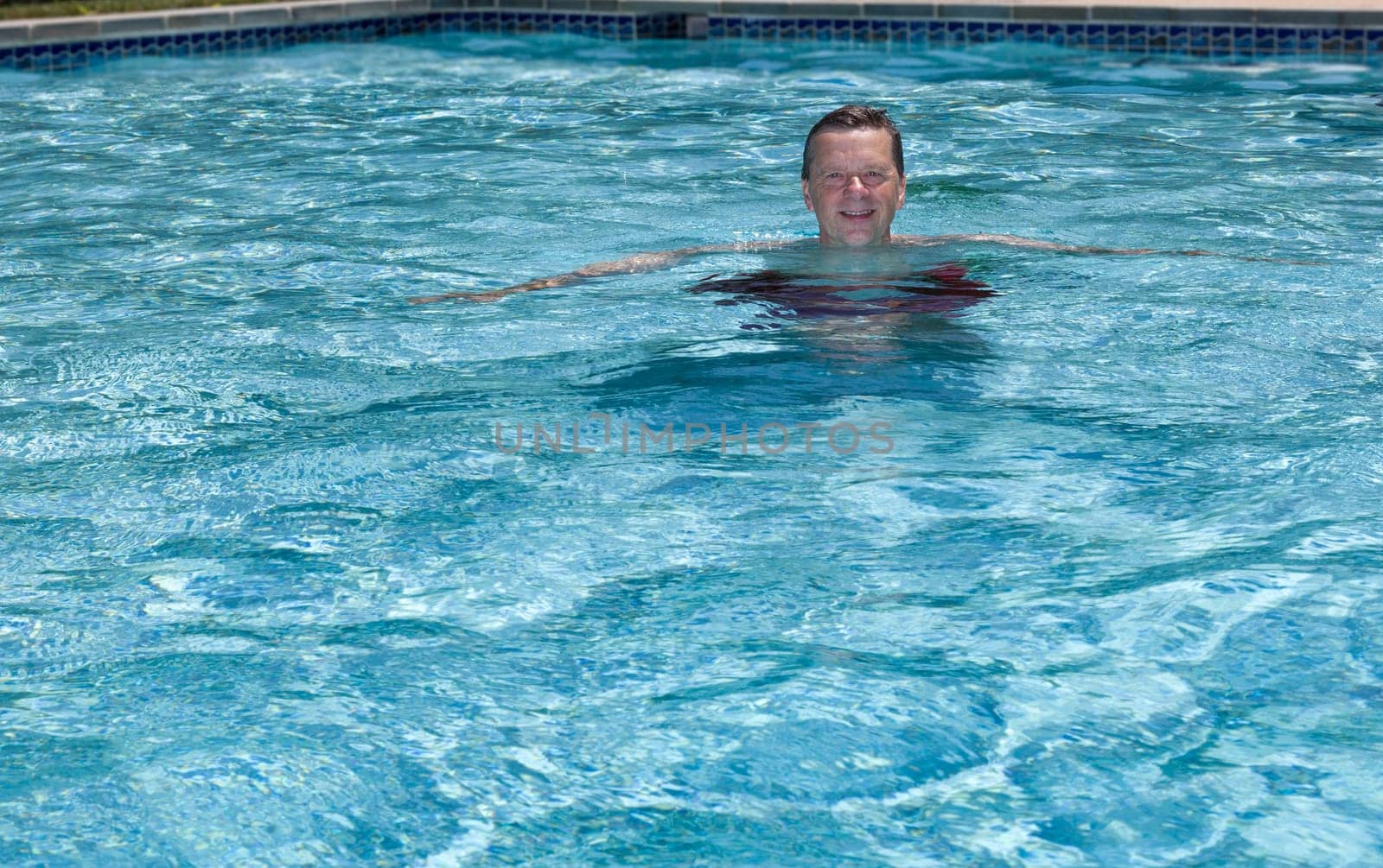 Baby boomer male floating in a backyard swimming pool on a hot summers day