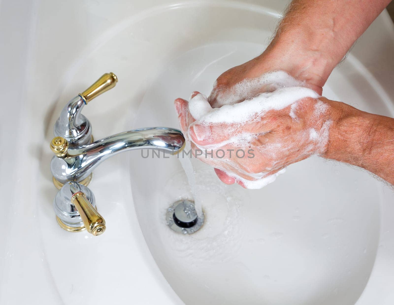 Senior man washing hands in modern sink with soap and lathering suds