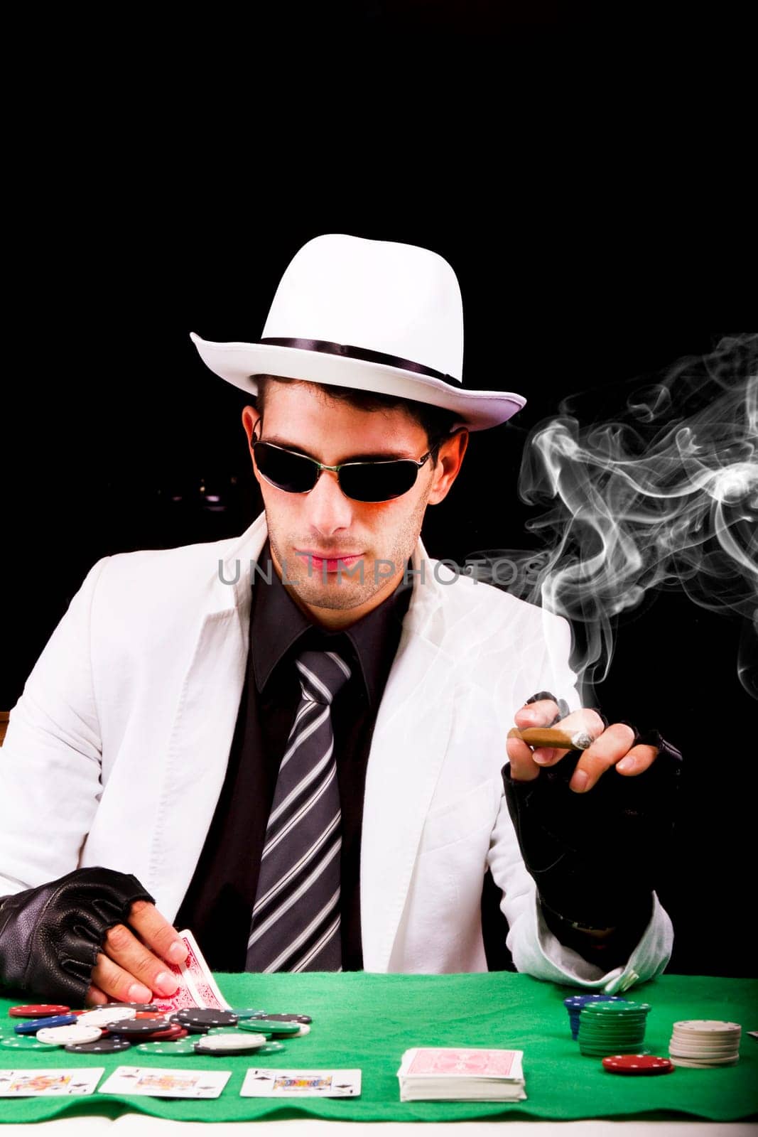 View of a gangster man playing some cards and poker, smoking a Cuban cigar.