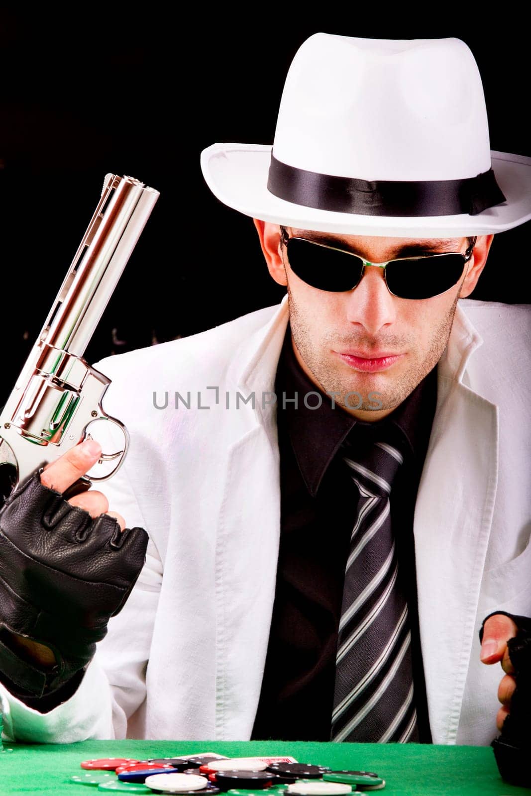 View of a gangster man playing some cards and poker, holding a gun.