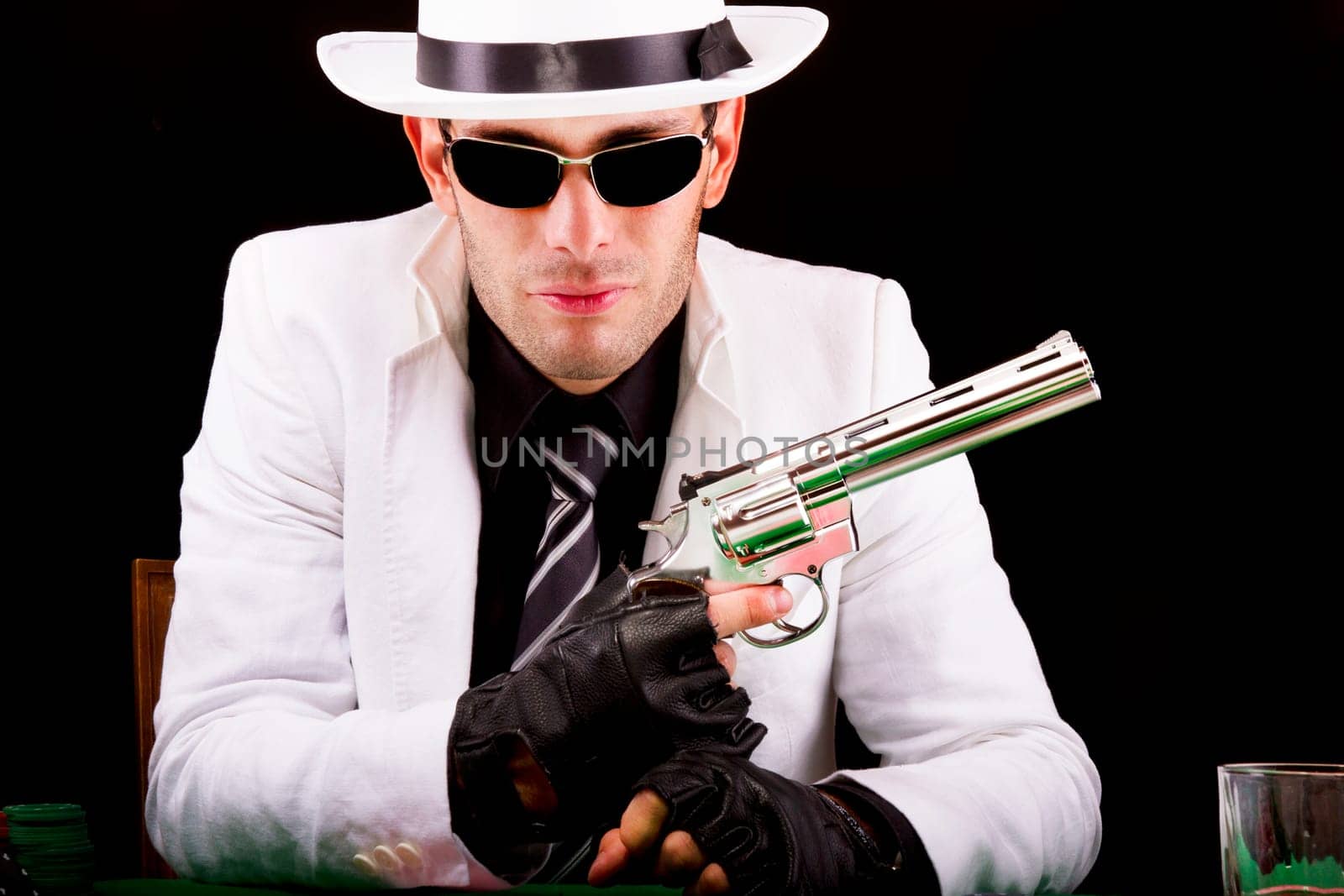 View of a gangster man playing some cards and poker, holding a gun.