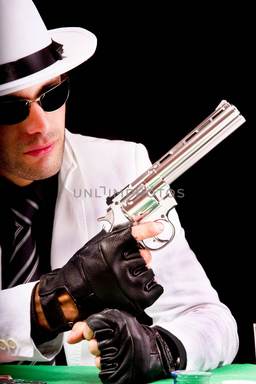 View of a gangster man playing some cards and poker,  holding a gun.