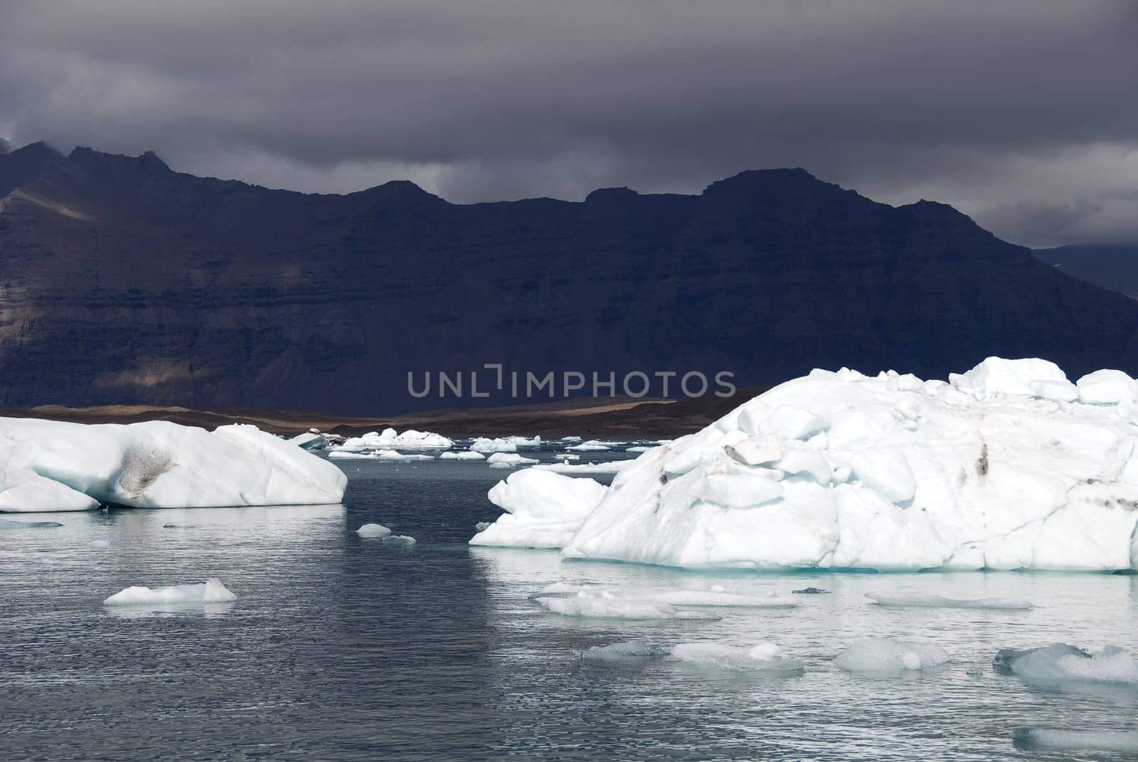 Iceberg reflections on the calm water of the lake Jokulsarlon with black mountains