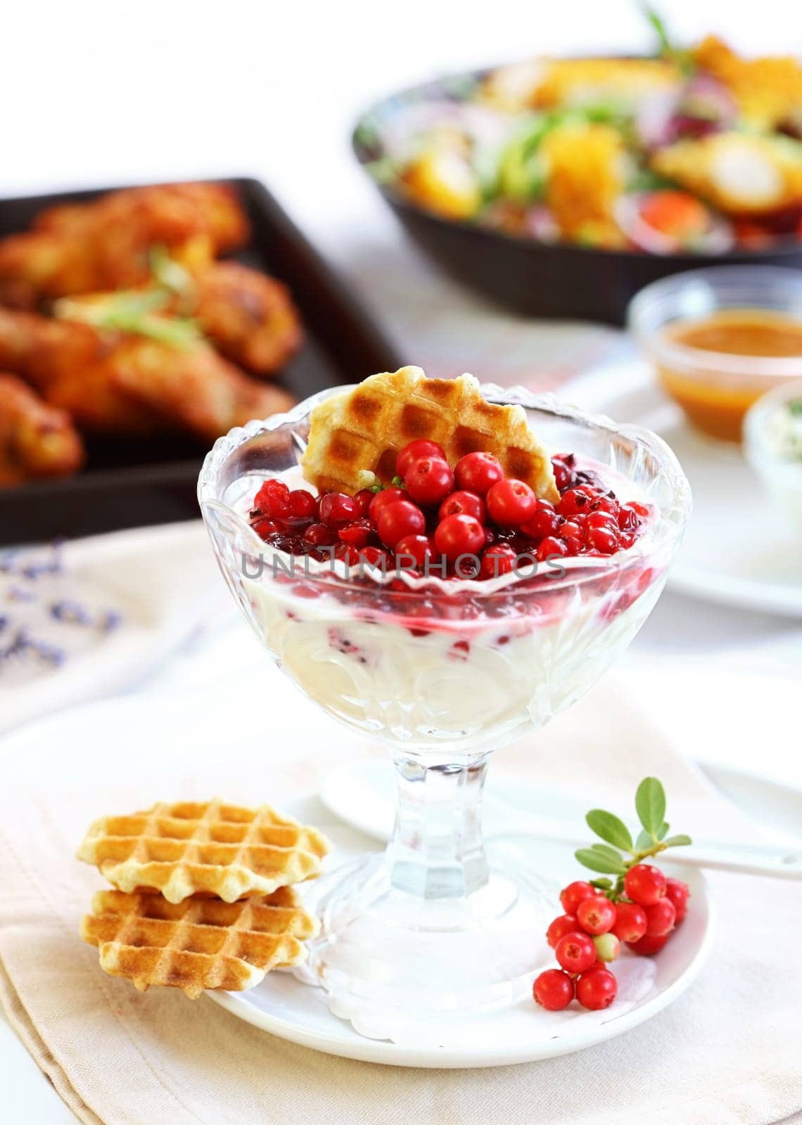 White yogurt with caramelized berries with chicken wings and vegetable salad in background