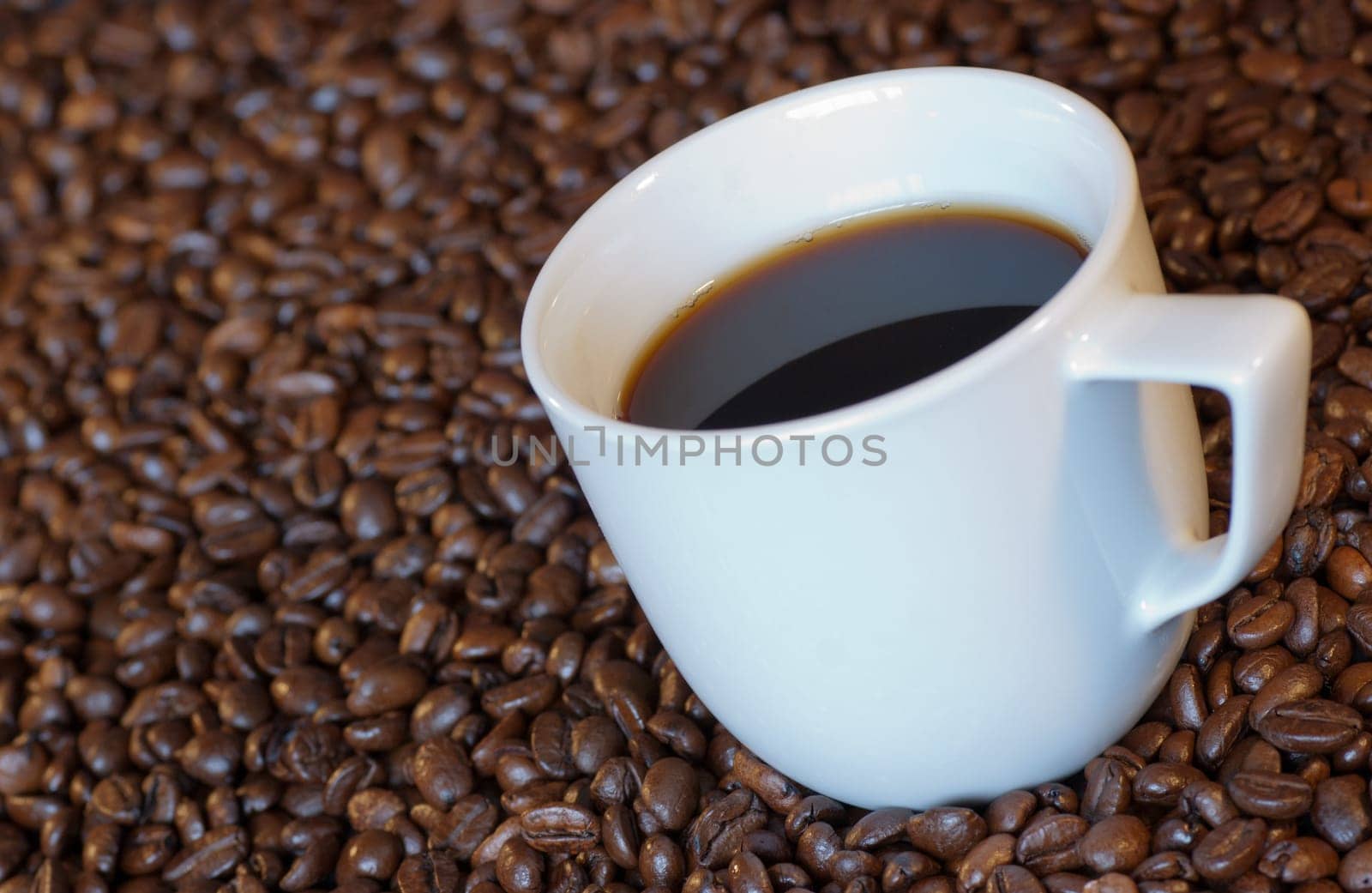 A cup of espresso surrounded by dark roasted coffee beans