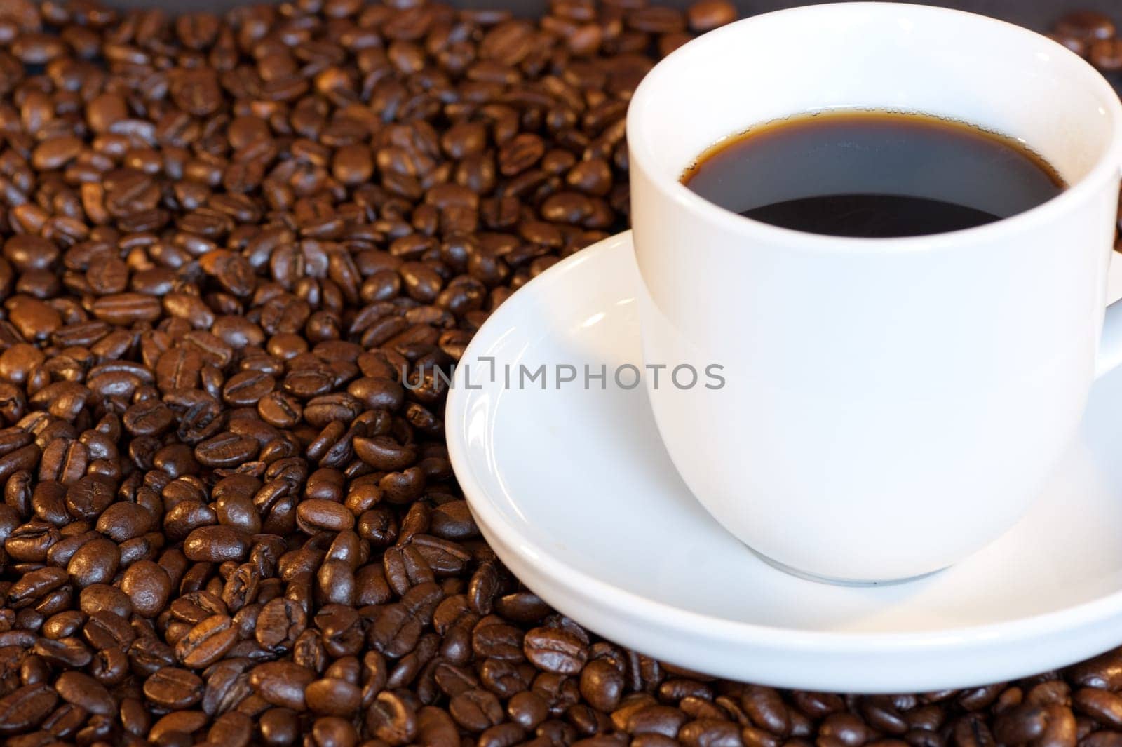 A white cup and saucer filled with black coffee among roasted coffee beans