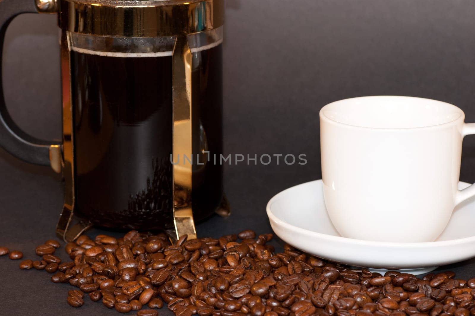 A jug of coffee with a white cup and saucer among coffee beans