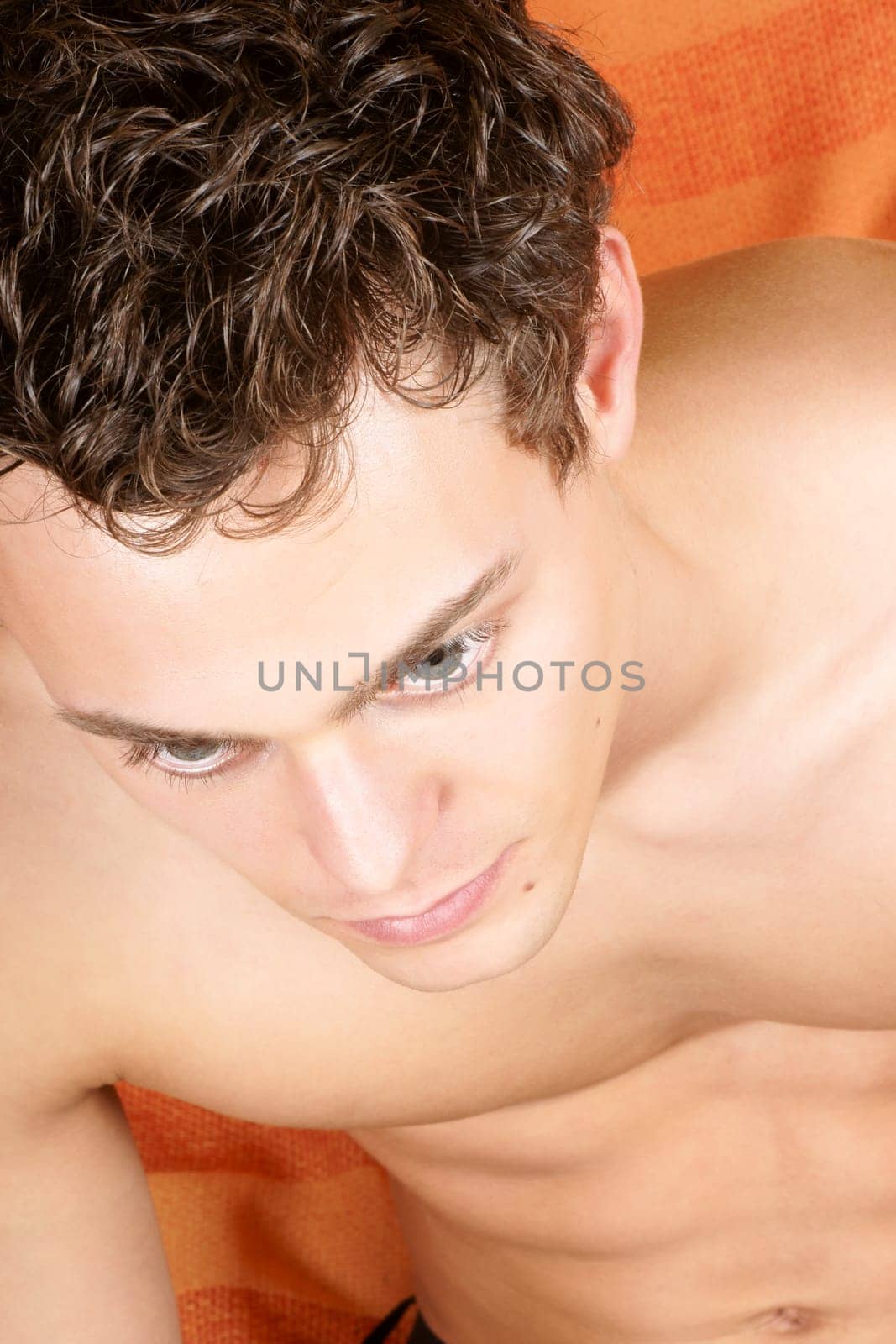 Sexy shirtless young man with brown hair and blue eyes over an orange fabric background.