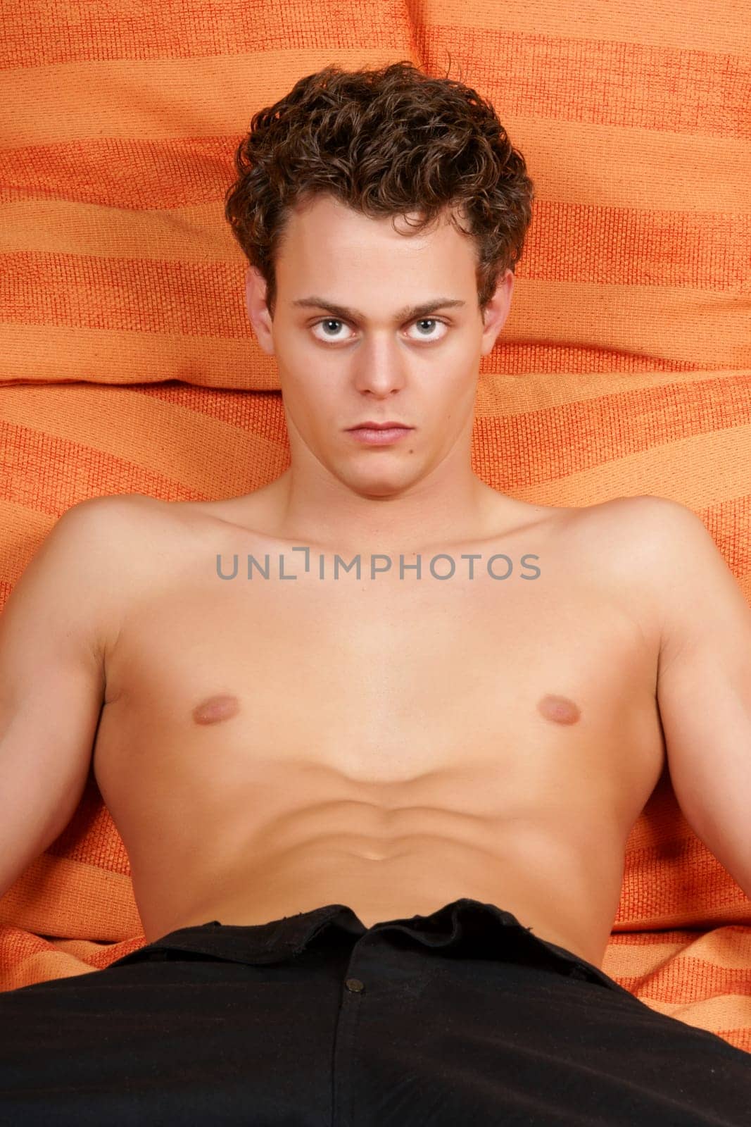 Sexy young man looking at camera among orange pillows