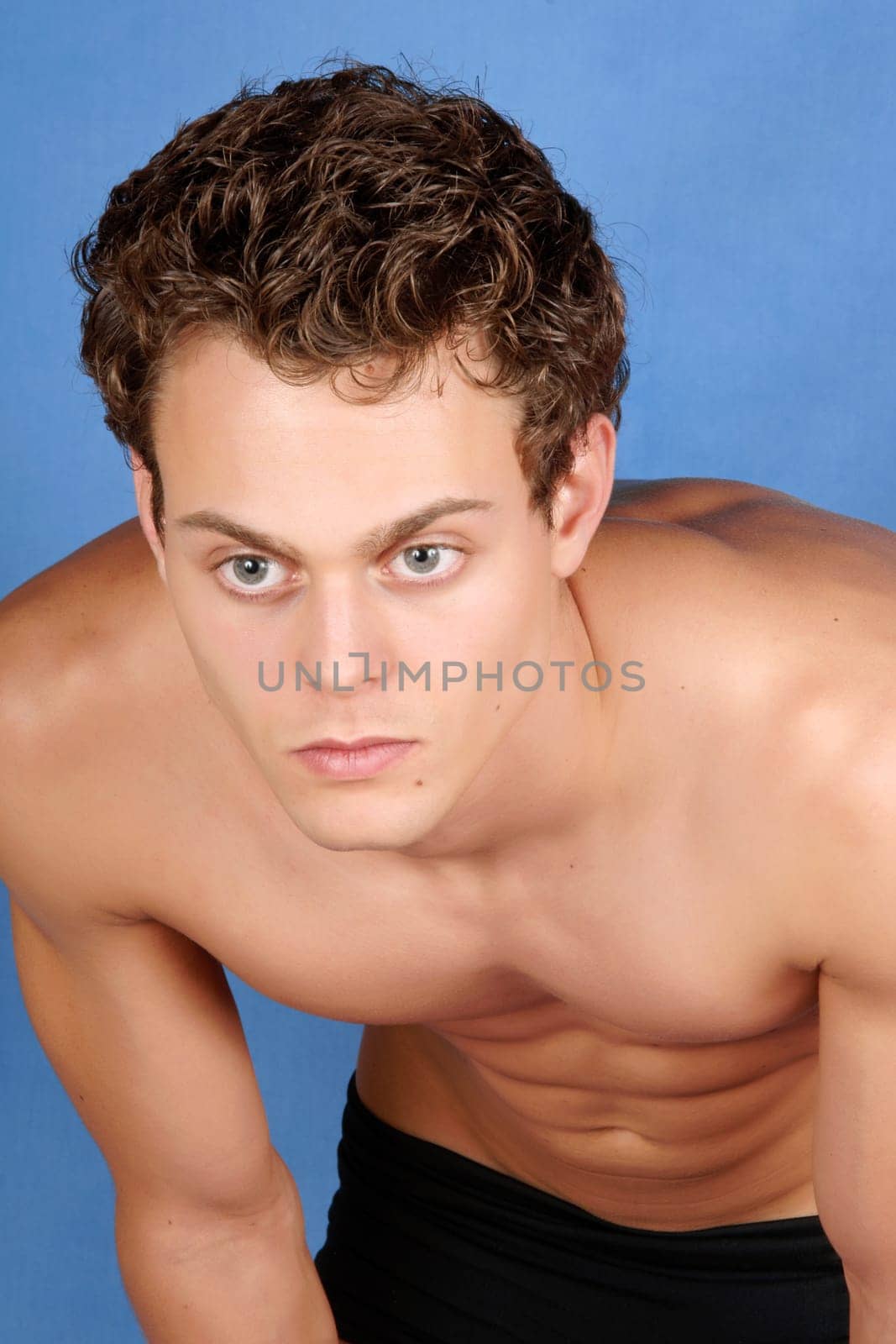 Sexy shirtless young man with blue eyes and brown hair over a blue background