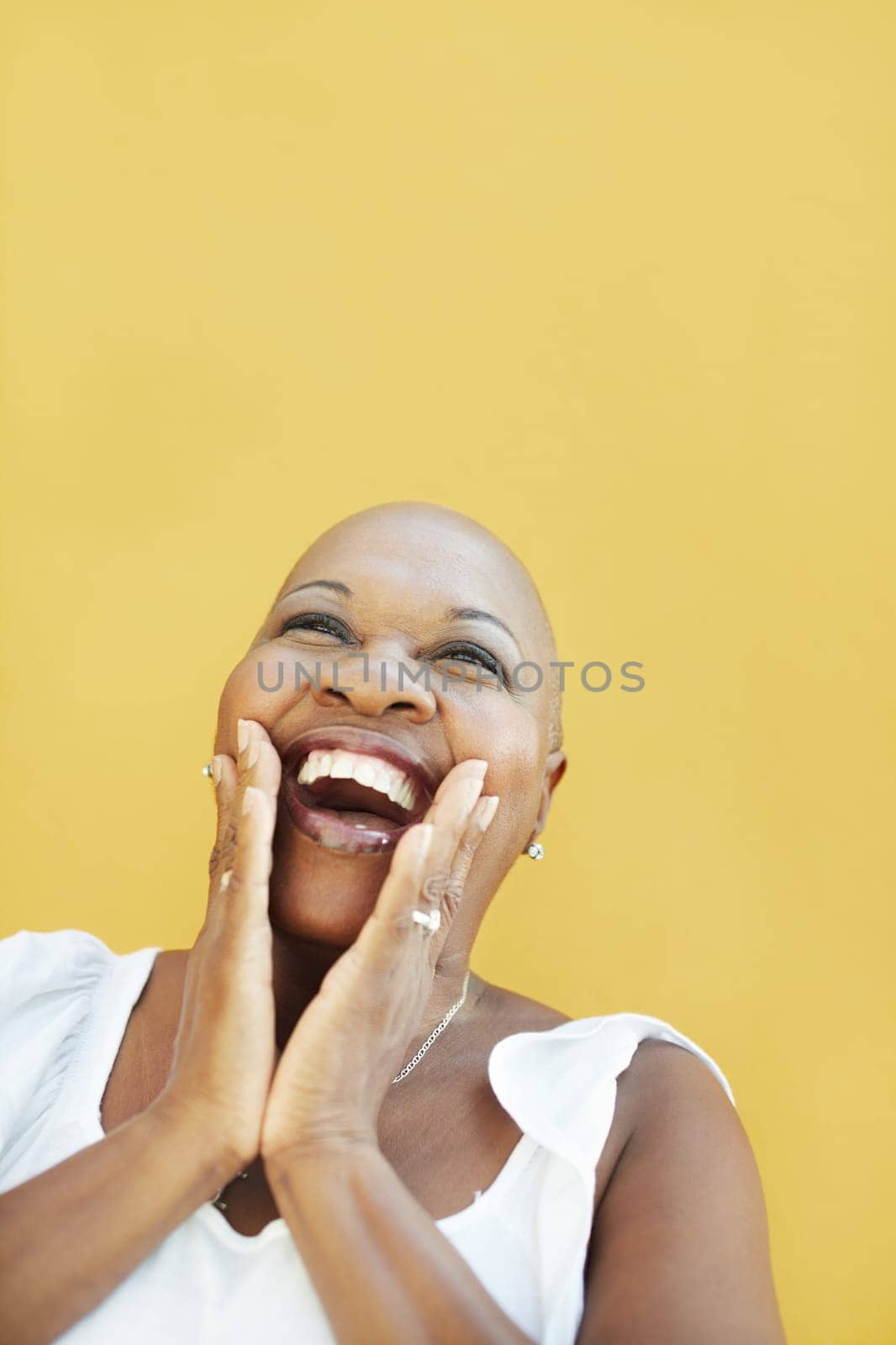 portrait of african 50 years old surprised woman with bald head, smiling on yellow background. Head and shoulders, copy space