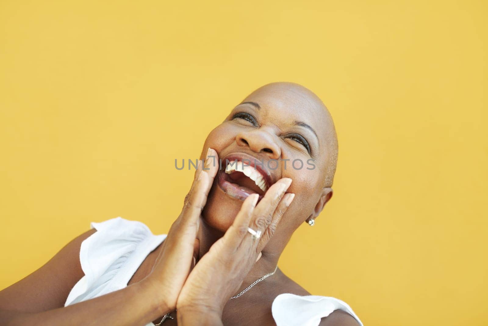 portrait of african 50 years old surprised woman with bald head, smiling on yellow background. Head and shoulders, copy space