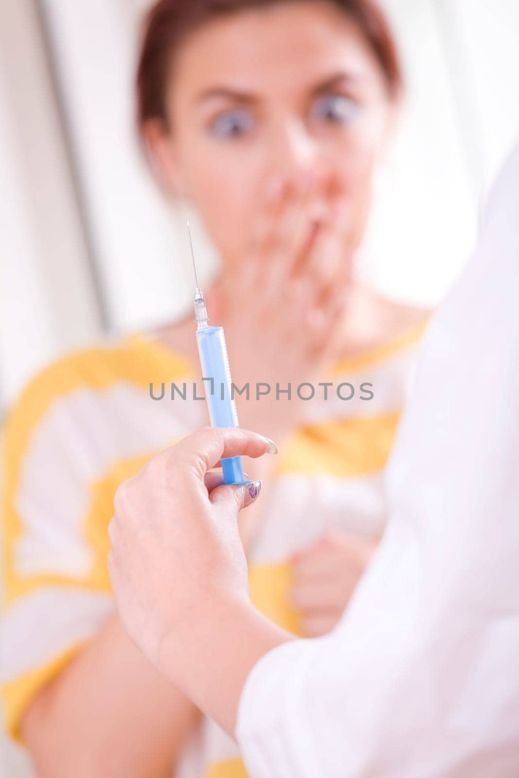 Doctor preparing vaccination injection - patient in fear on background. Focus on syringe and hand.