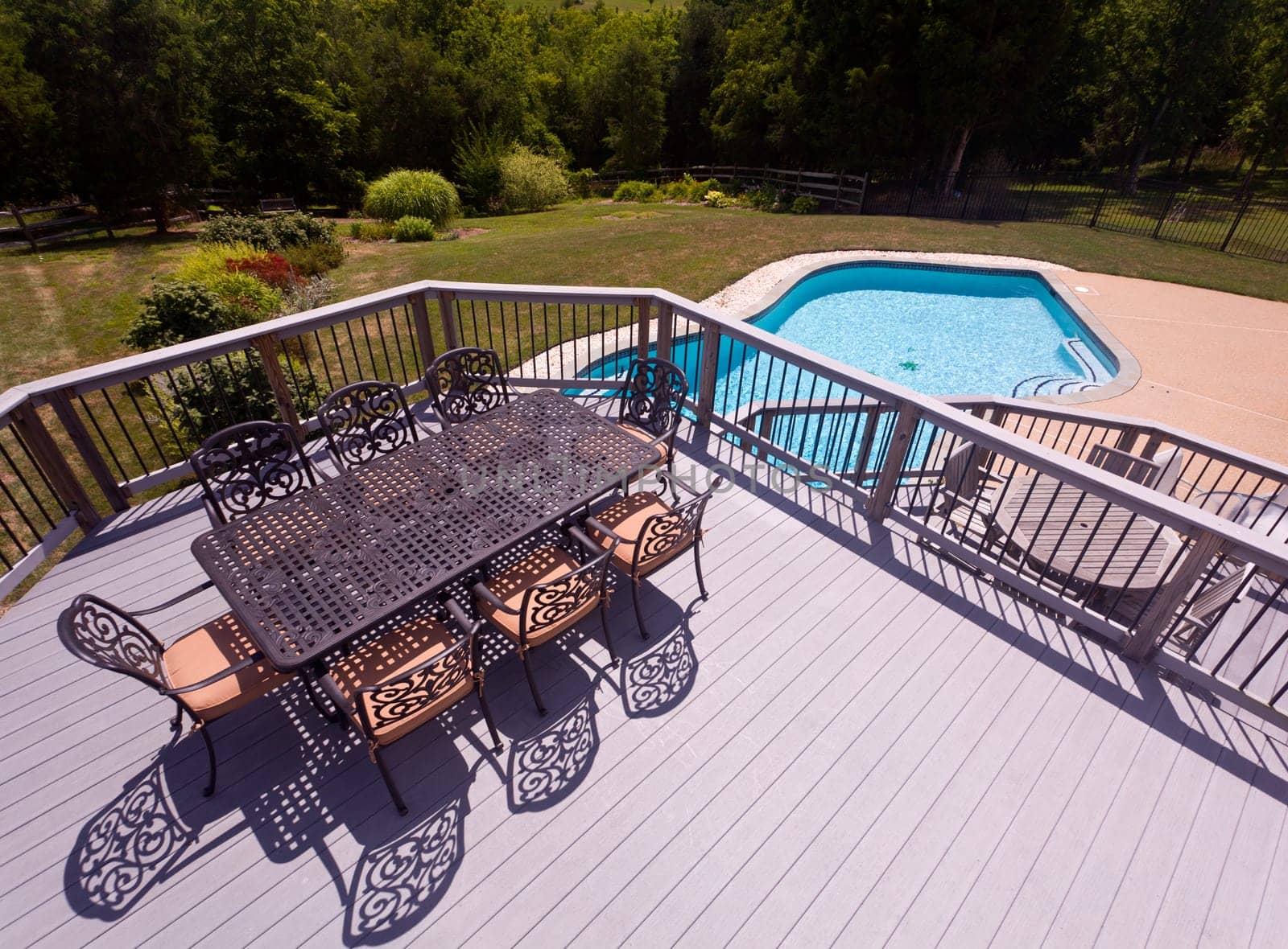 Modern table and chairs on wooden deck with swimming pool in back yard garden setting