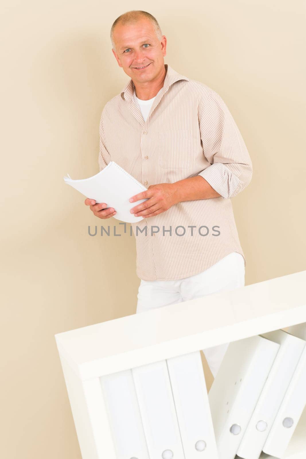 Casual businessman mature standing behind bookshelf hold paper