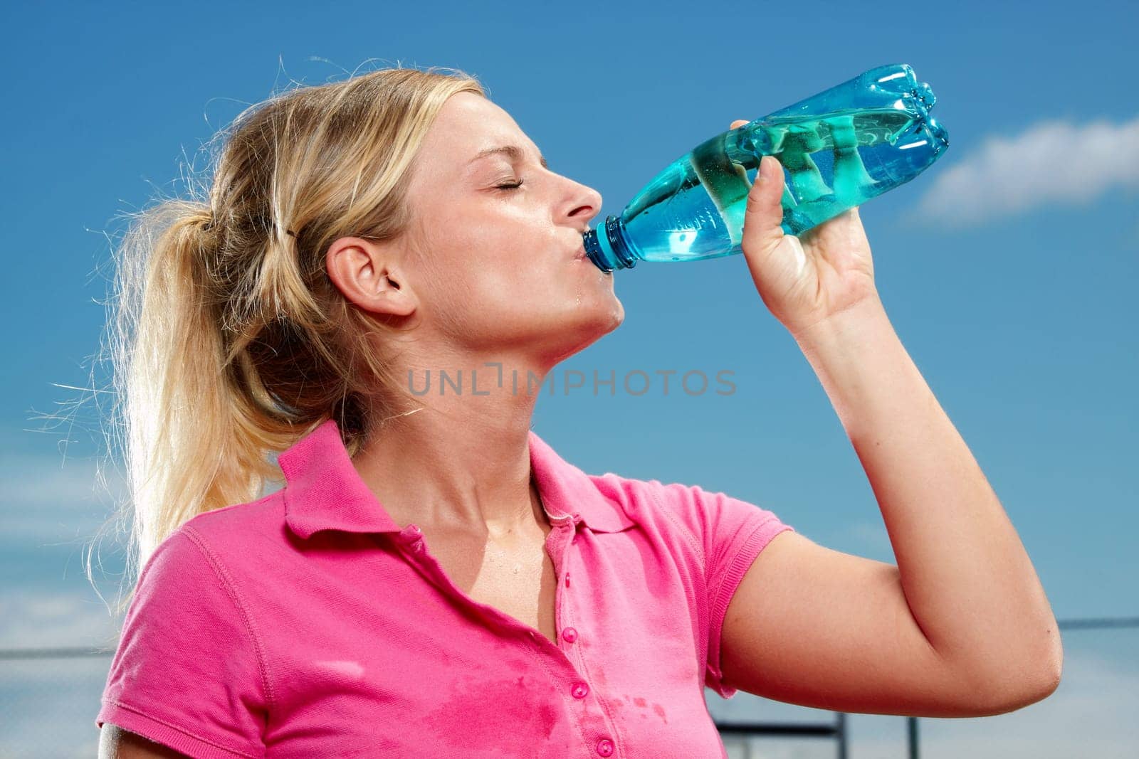 Young thirsty woman drinking water on sports field