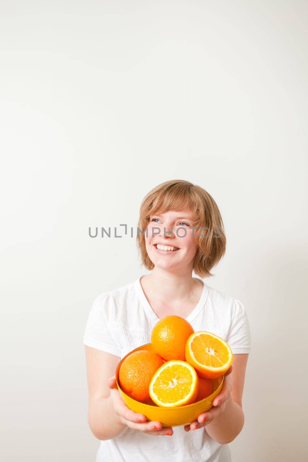 Young woman holding a bowl of fresh oranges. Studio shot.