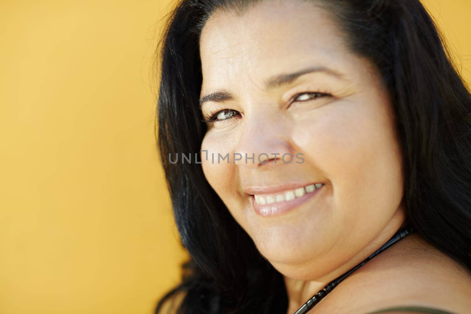portrait of latin american 50 years old overweight woman smiling on yellow background. Head and shoulders, copy space