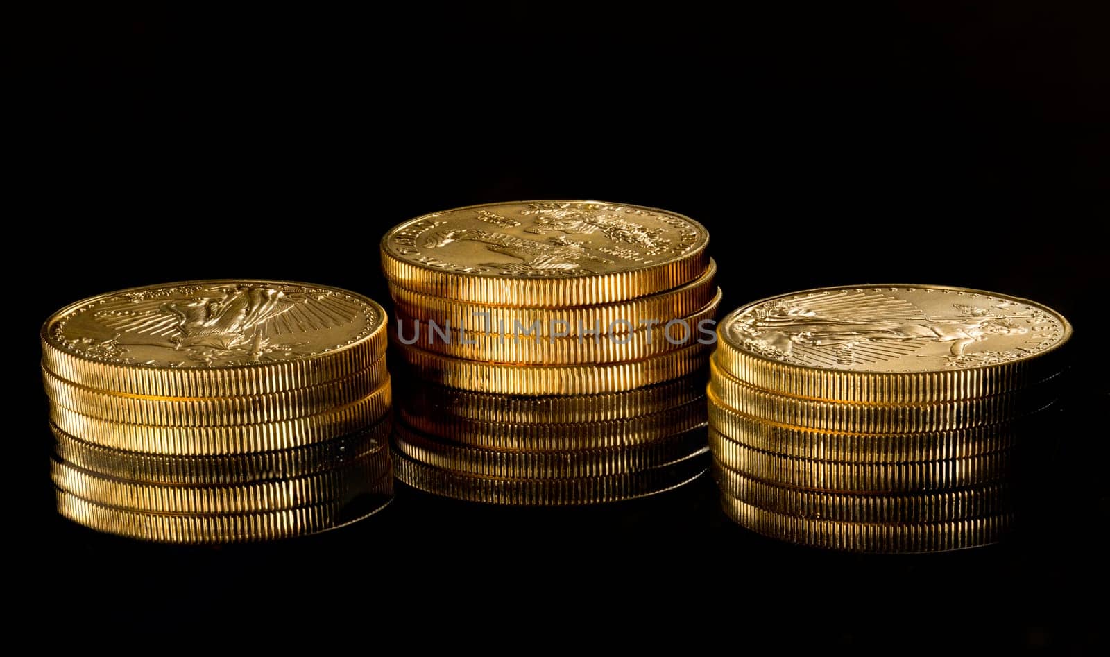 Close up of a solid gold eagle one ounce coin stacked on other coins and reflected in black surface
