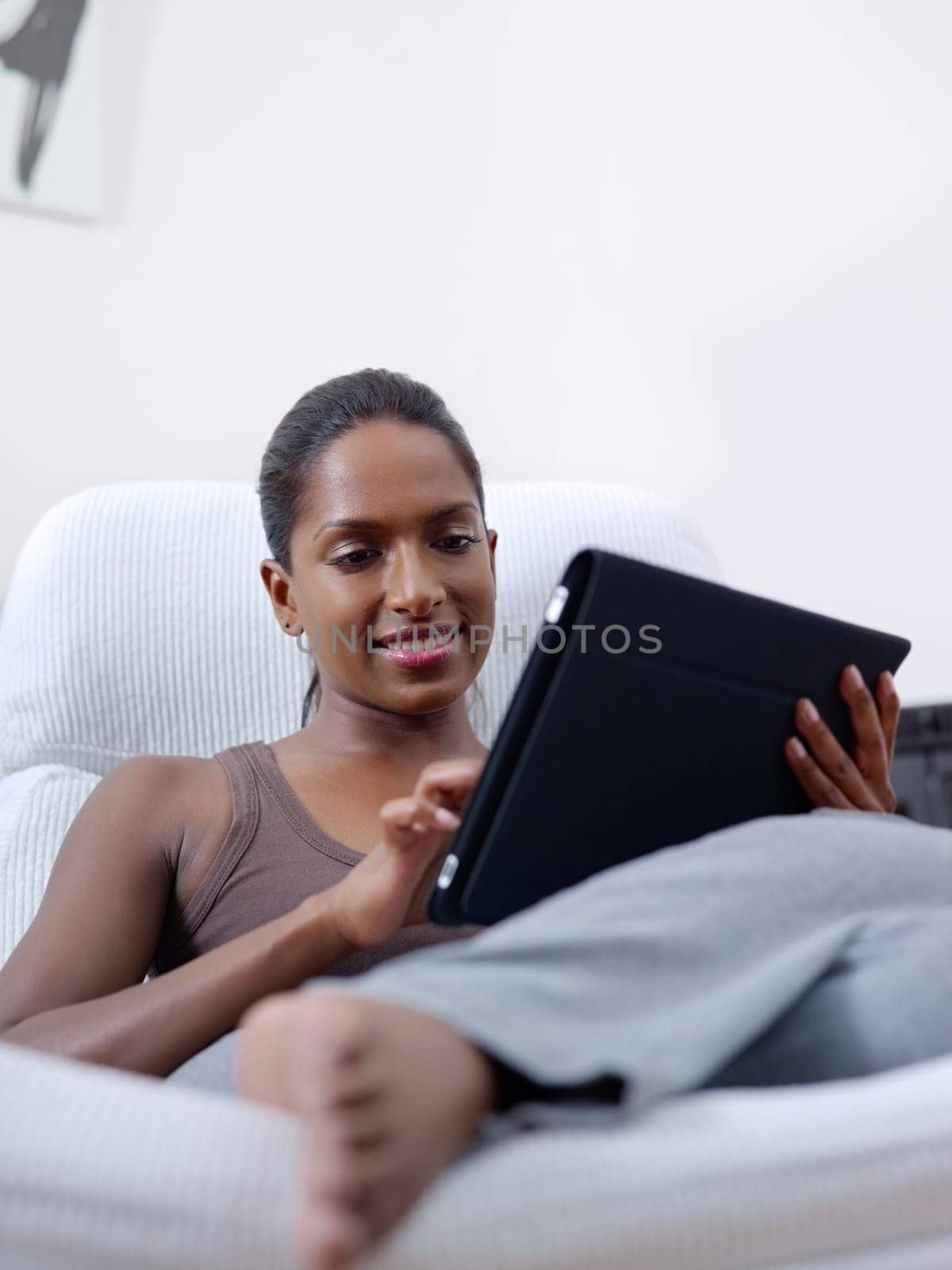 mid adult indian woman relaxing on armchair and using touch pad computer. Vertical shape, front view, copy space