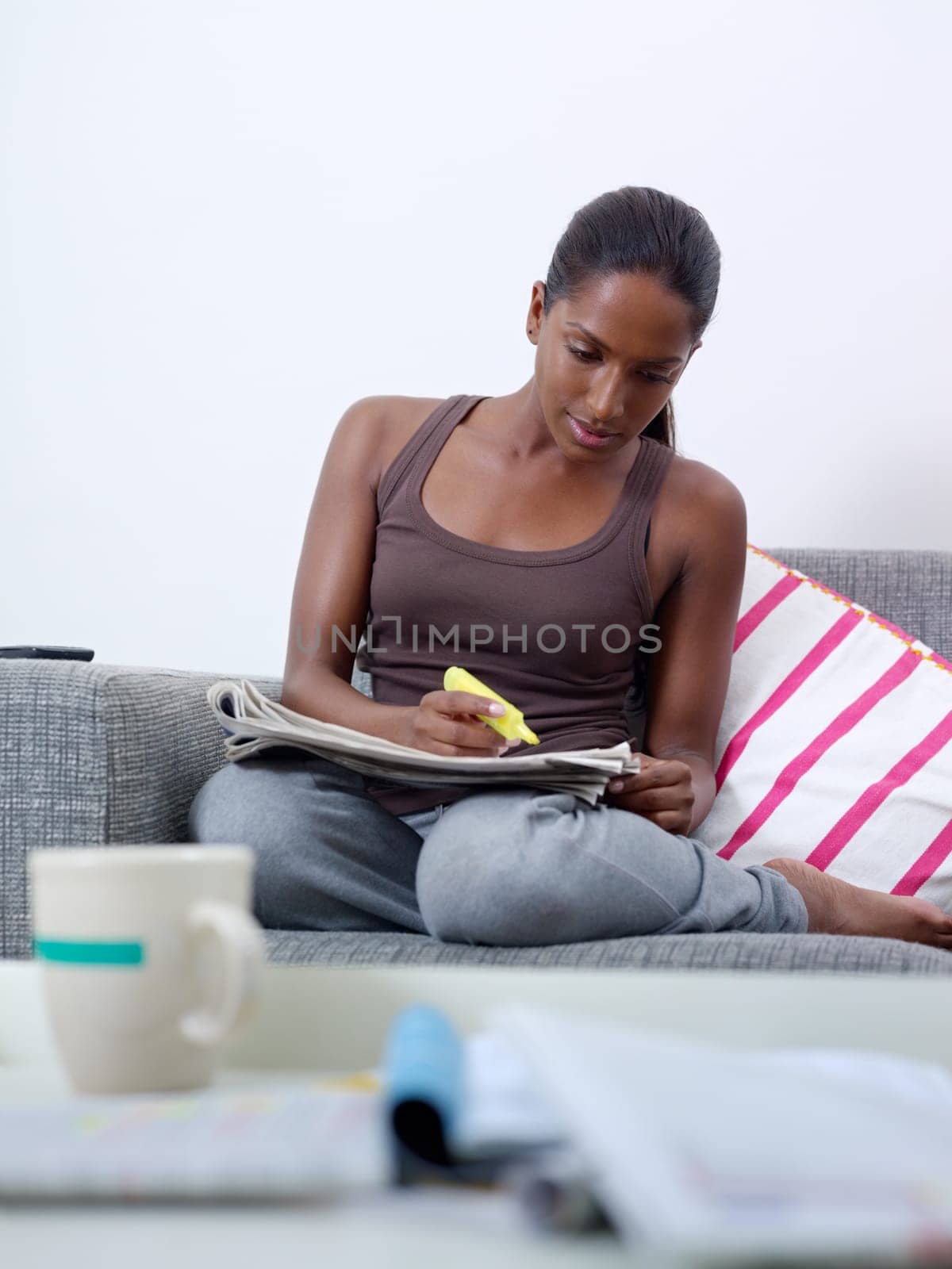 mid adult indian woman on sofa, looking for job offers on newspapers. Front view, copy space