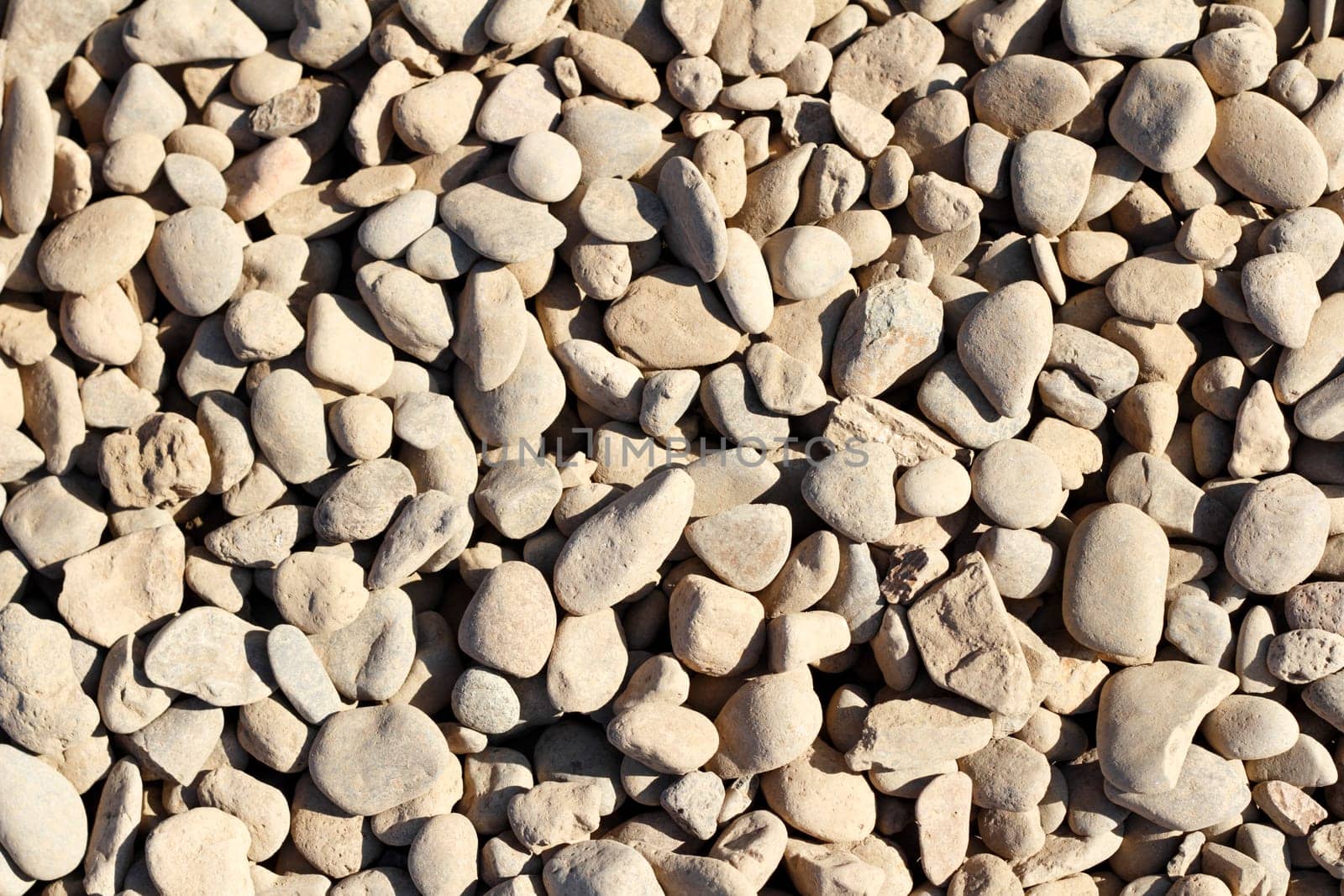 Small tan dirt dusty gray river rock background outdoor in the summer sun.