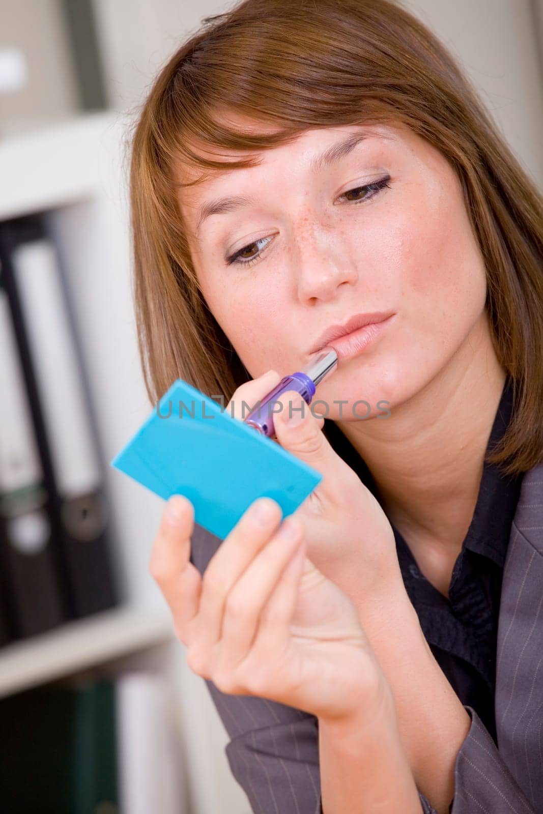 young woman putting on makeup by office work