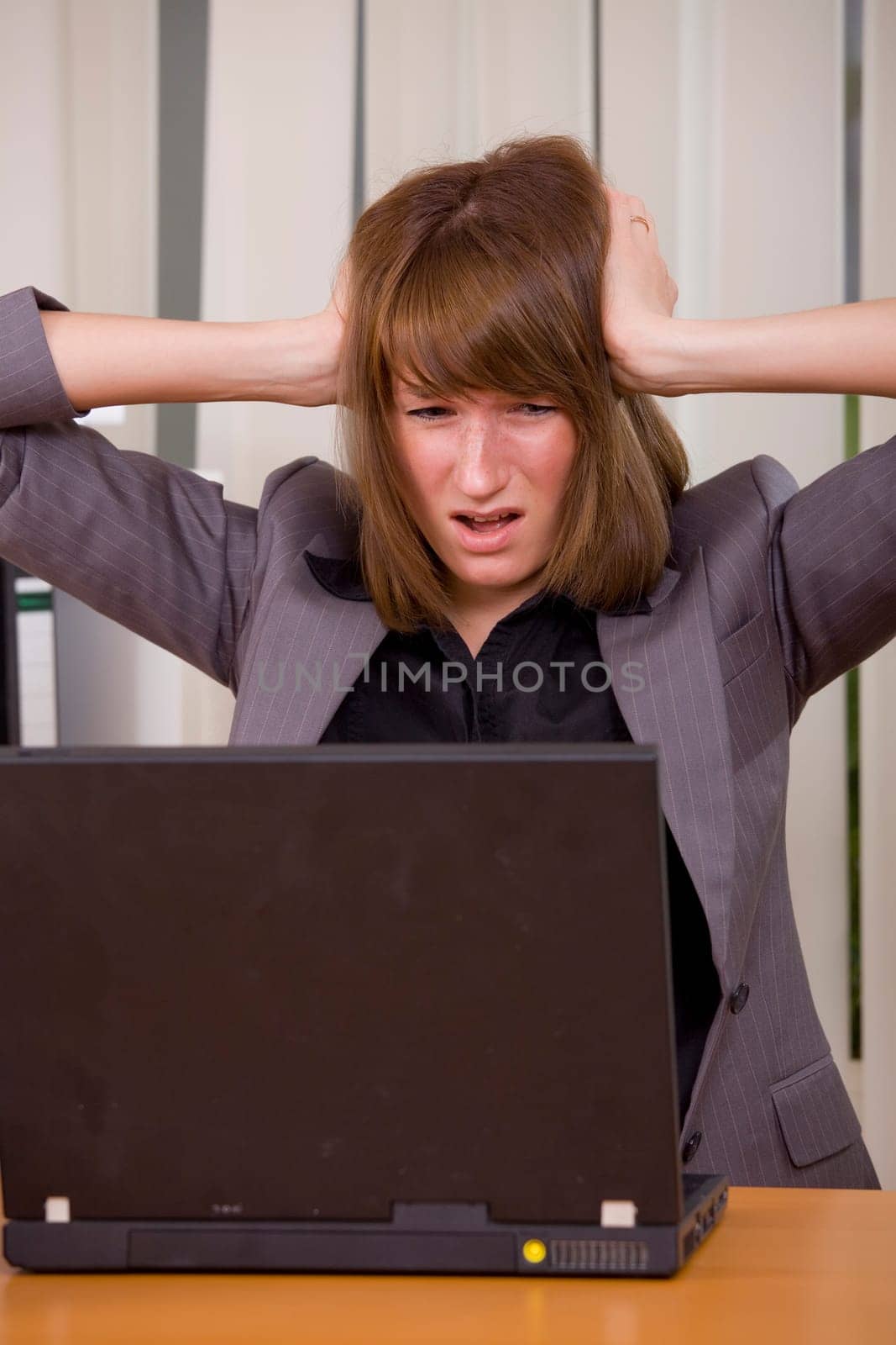 stressed businesswoman holding her head with both hands looking at laptop