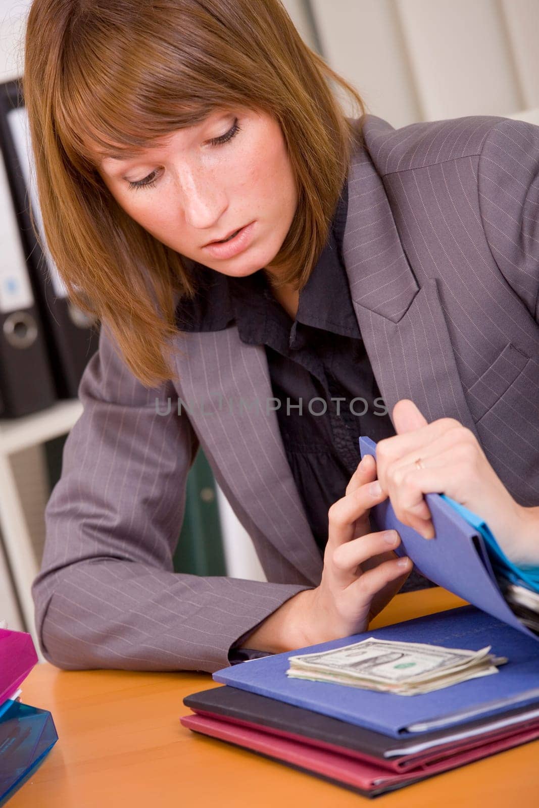 young surprised woman looking at money hidden between files