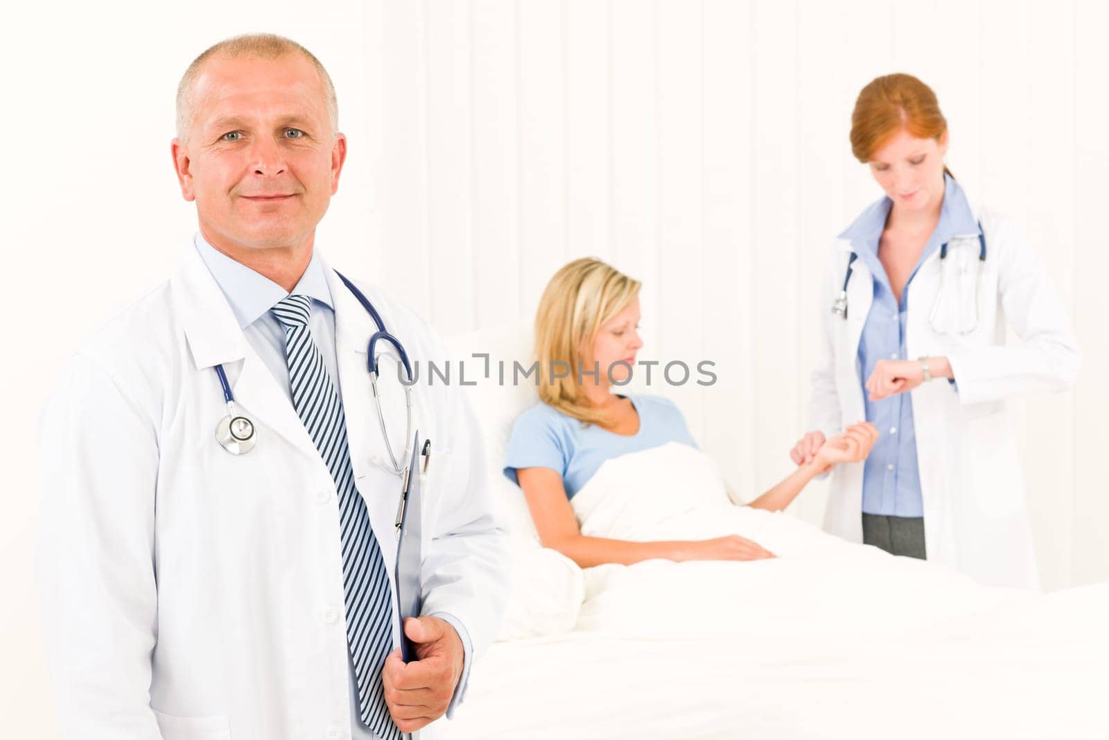 Two medical doctors with patient lying in bed examine pulse