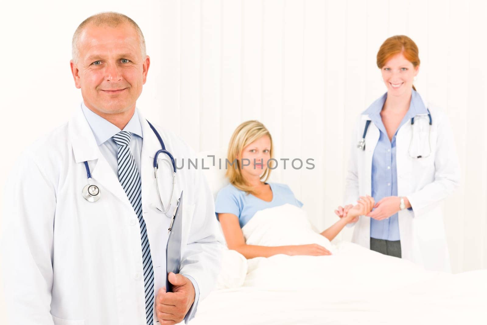 Two medical doctors with patient lying in bed examine pulse