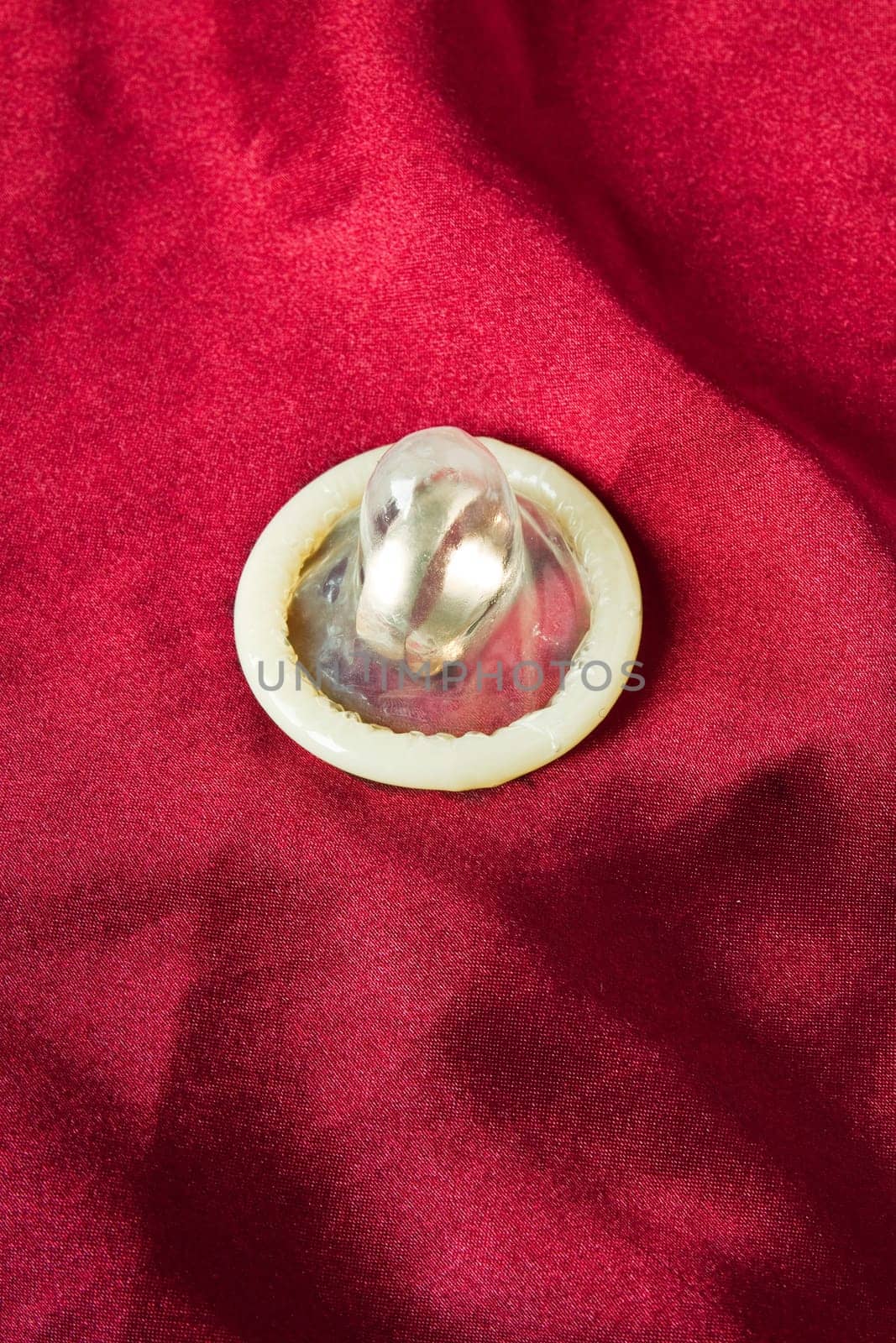 Wedding ring condom in a red satin background