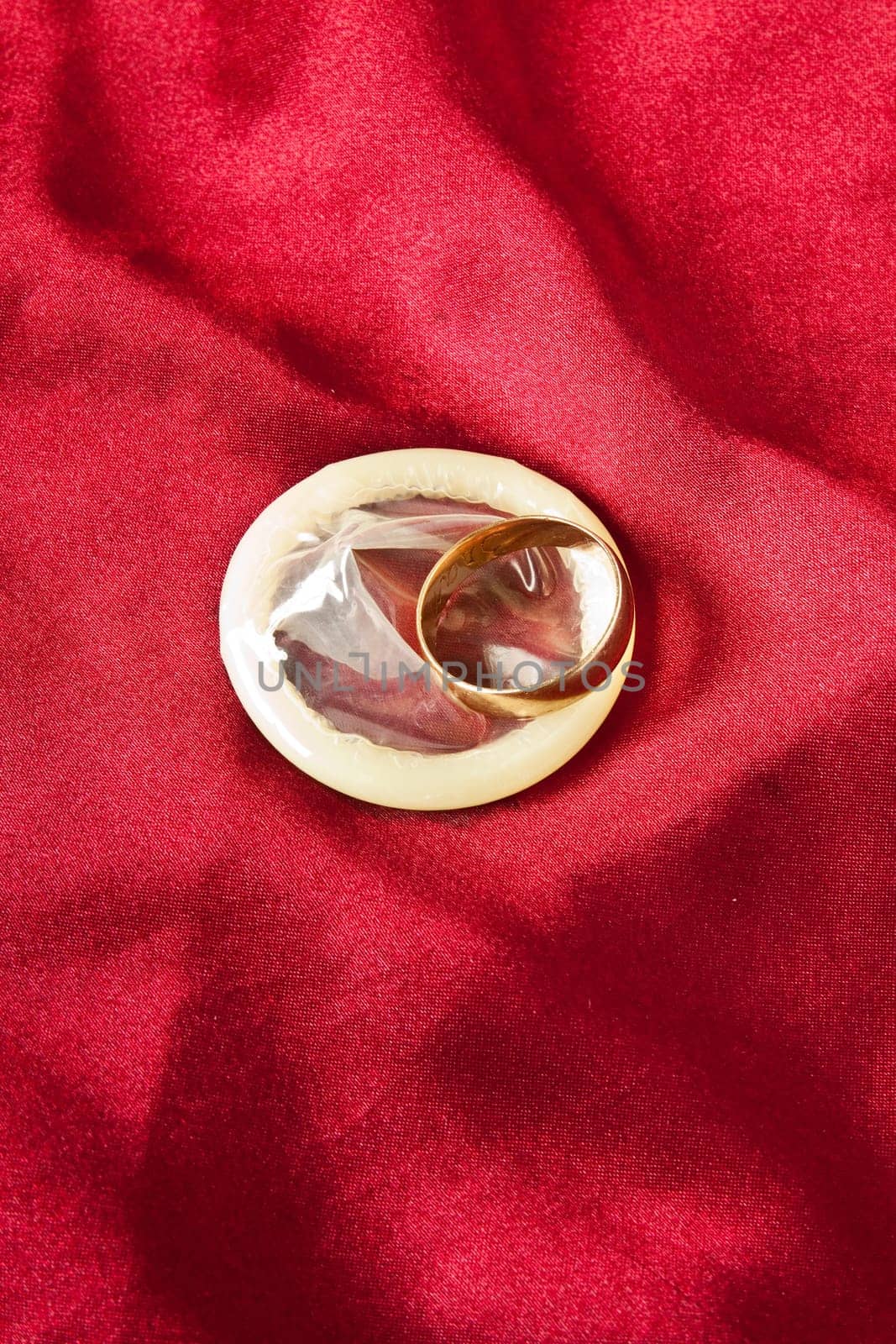 Wedding ring on the condom against the red satin