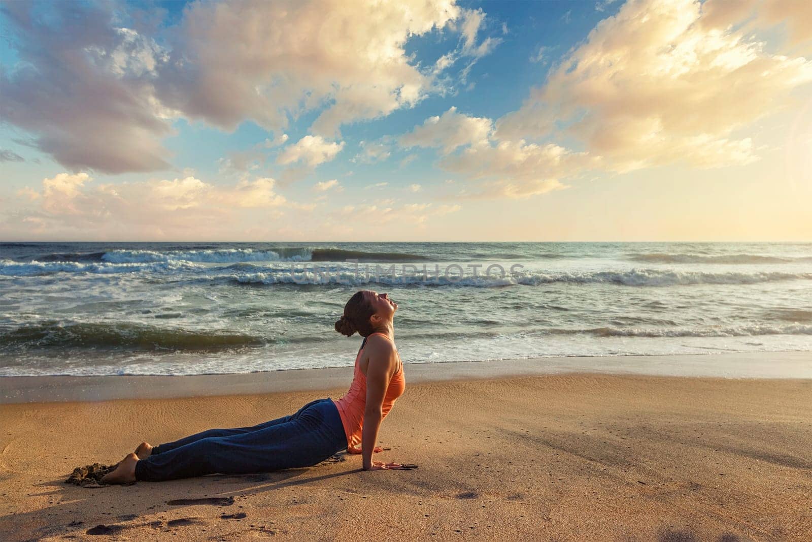 Woman practices yoga asana Urdhva Mukha Svanasana at the beach by dimol