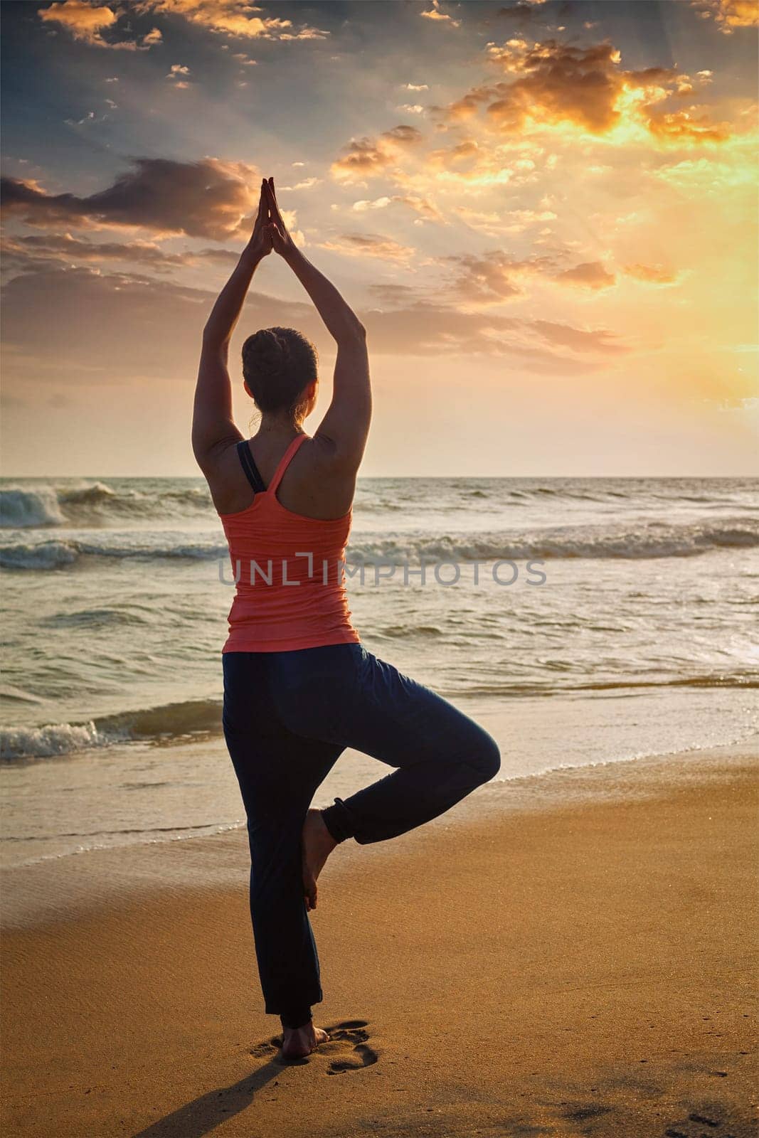 Young sporty fit woman doing yoga tree asana on beach by dimol