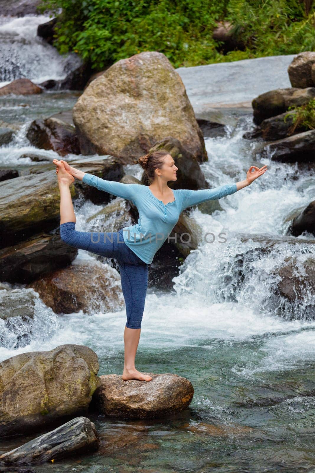 Yoga outdoors - woman doing yoga asana Natarajasana - Lord of the dance balance pose outdoors at waterfall in Himalayas
