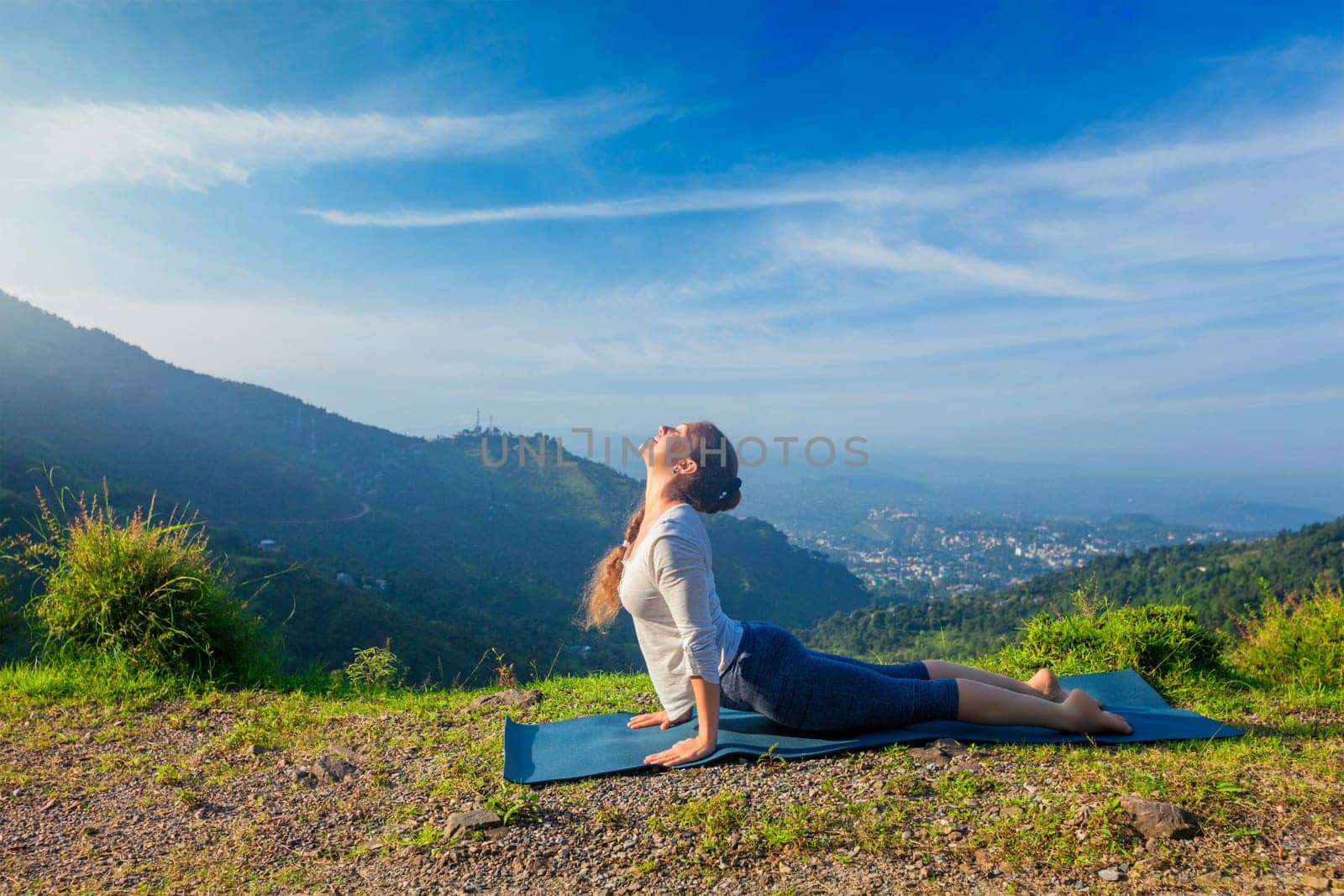 Yoga outdoors - woman practices Ashtanga Vinyasa yoga Surya Namaskar Sun Salutation asana Urdhva Mukha Svanasana - upward facing dog pose in mountains in the morning