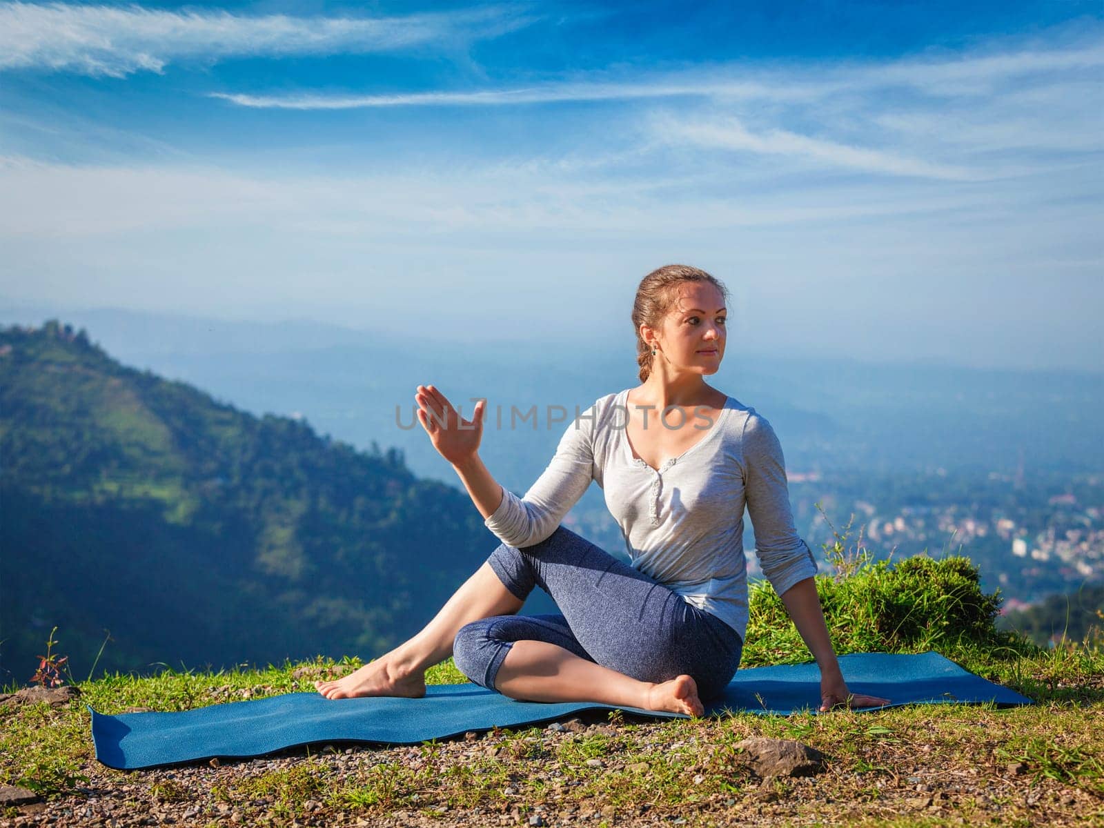 Yoga exercise outdoors - woman doing Ardha matsyendrasanaasana asana - half spinal twist pose mountains in Himalayas in India in the morning