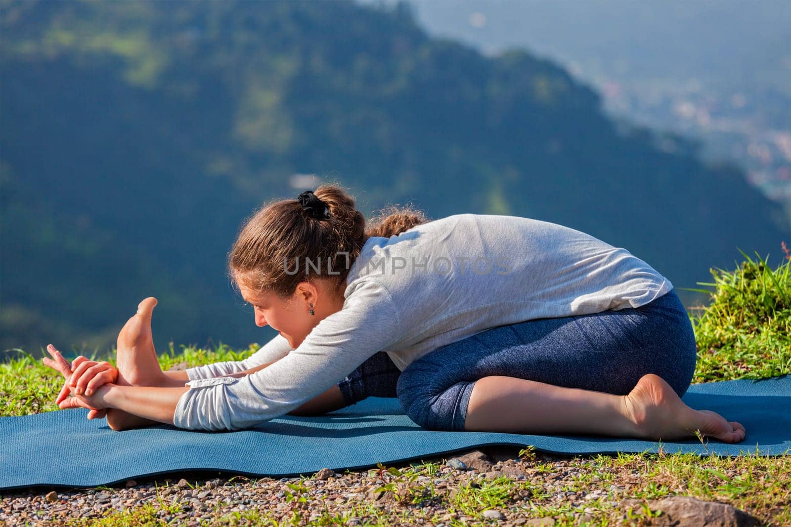 Yoga outdoors - woman doing Ashtanga Vinyasa yoga Tiryam-Mukha Eka-Pada Paschimottanasana asana stretching position outdoors