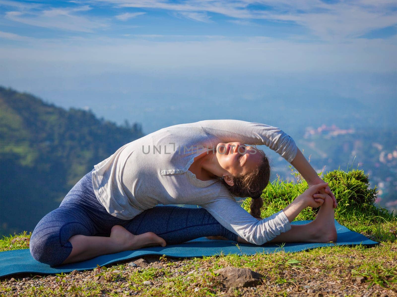 Yoga outdoors - young sporty fit woman doing Hatha Yoga asana parivritta janu sirsasana - Revolved Head-to-Knee Pose - in mountains in the morning
