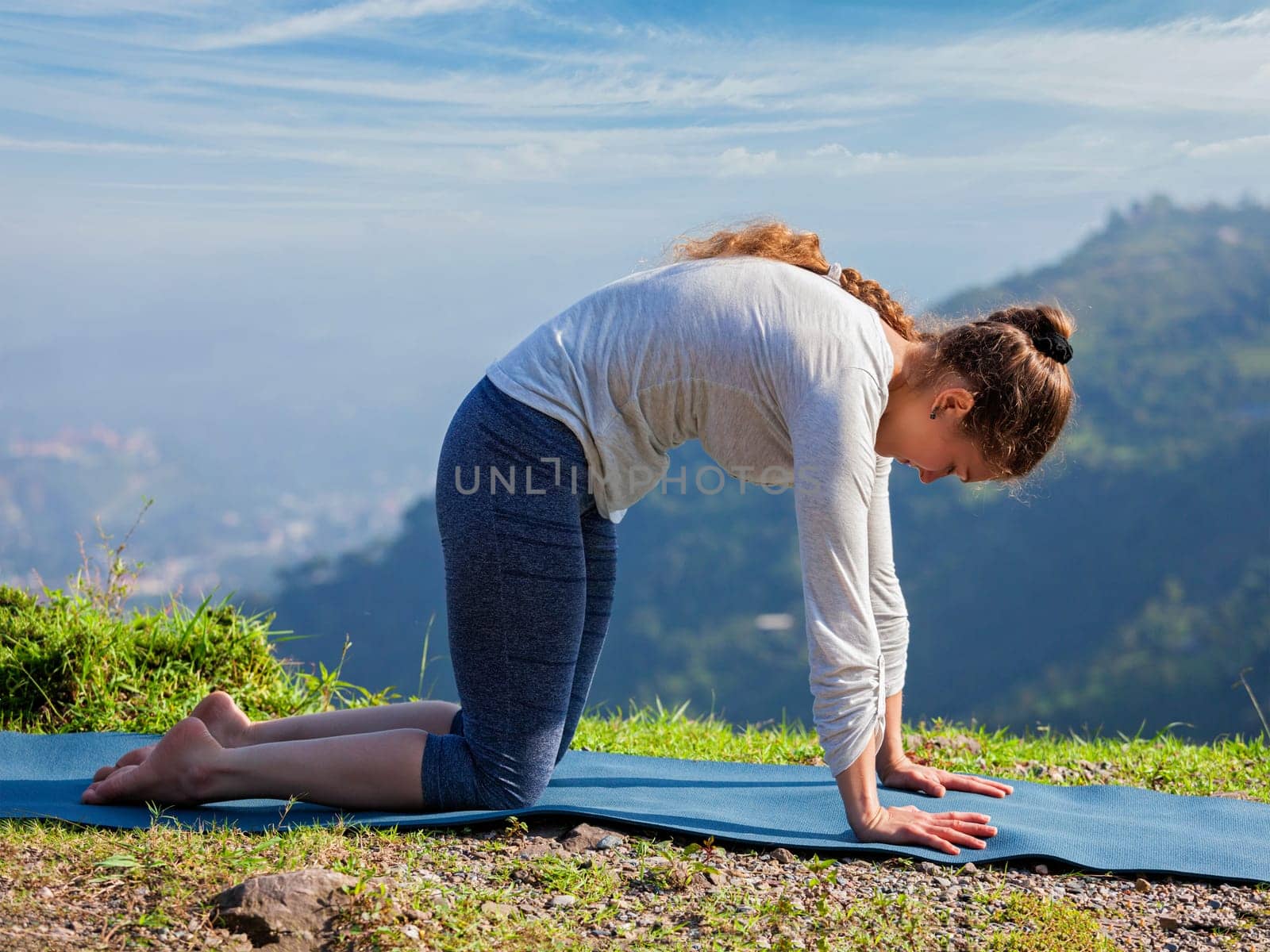 Sporty fit woman practices yoga asana Marjariasana outdoors by dimol