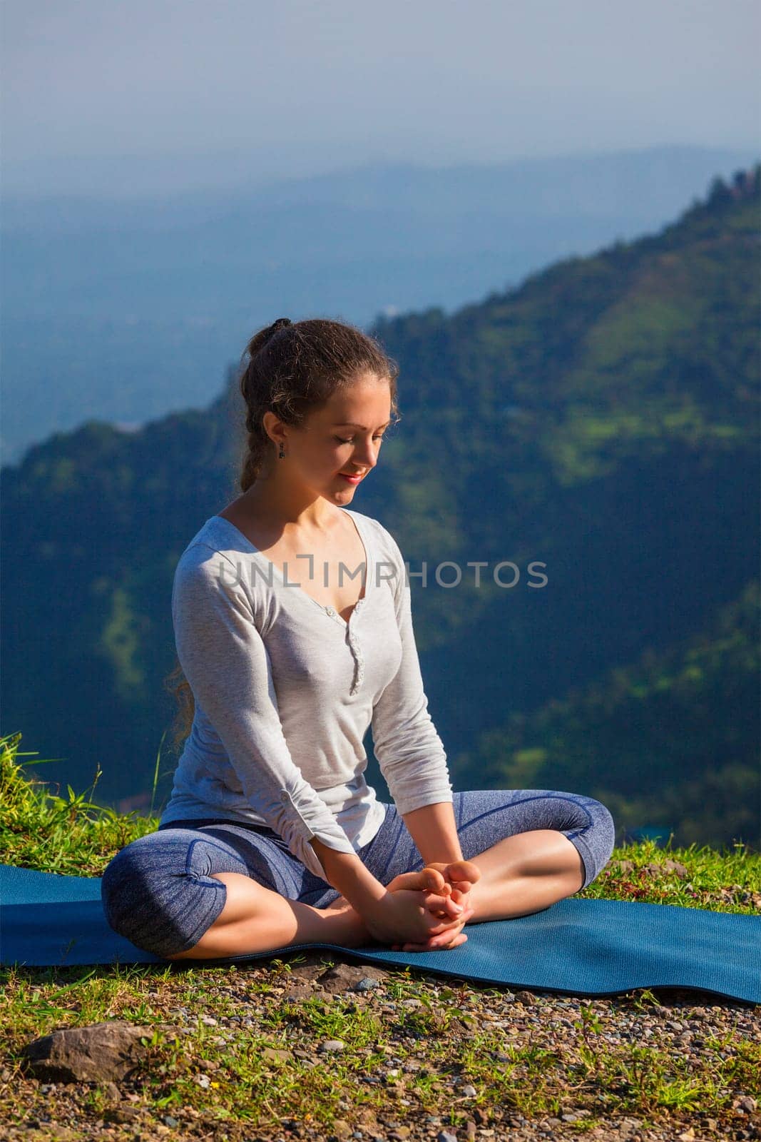 Sporty fit woman practices yoga asana Baddha Konasana - bound angle pose outdoors in HImalayas mountains in the morning with sky. Himachal Pradesh, India