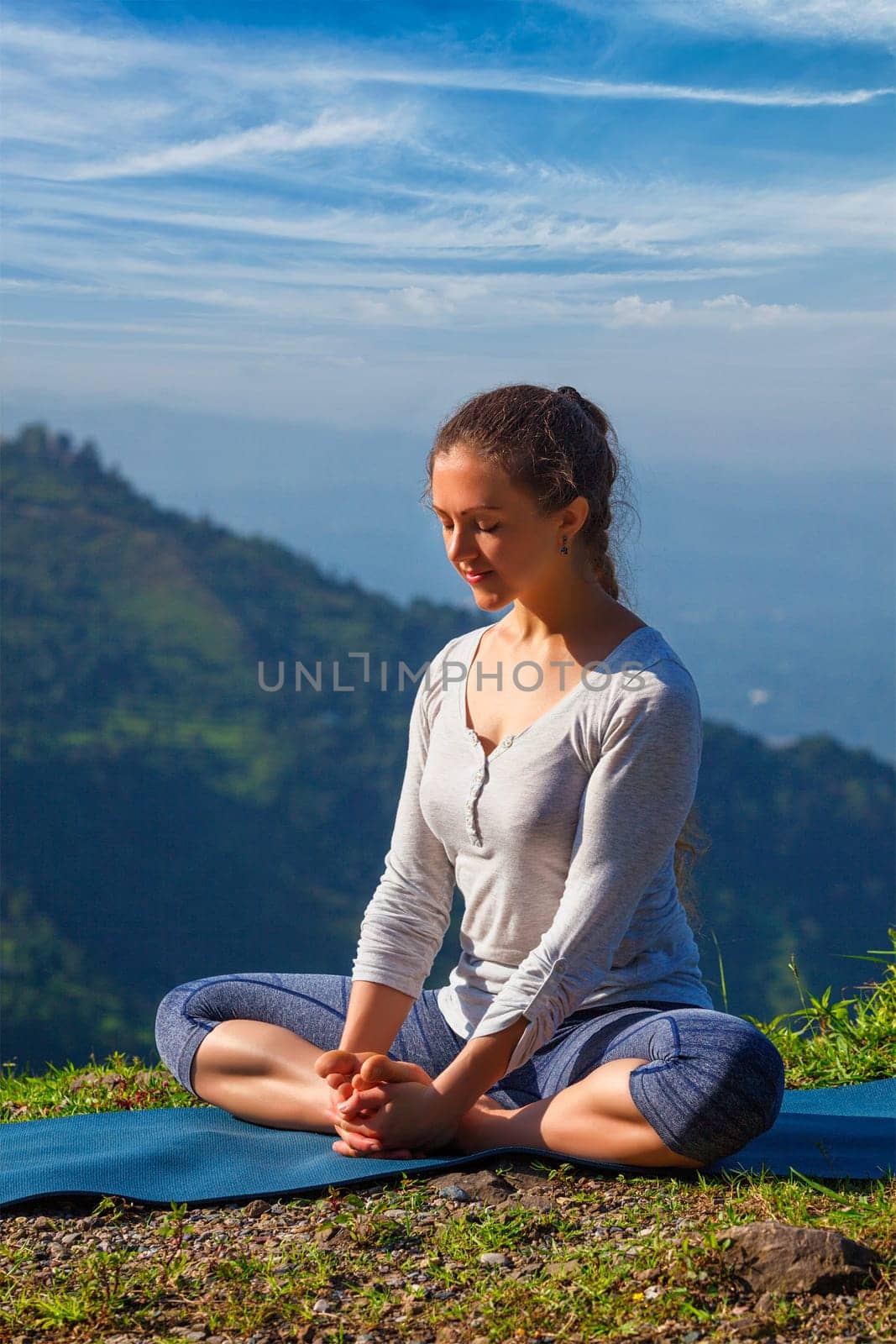 Sporty fit woman practices yoga asana Baddha Konasana - bound angle pose outdoors in HImalayas mountains in the morning with sky. Himachal Pradesh, India