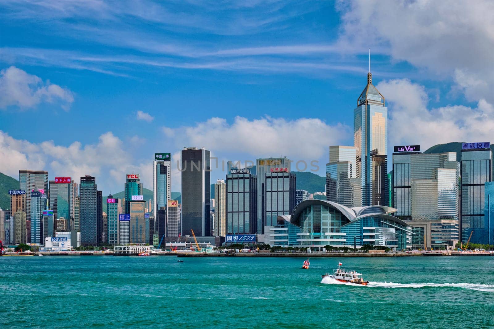 HONG KONG, CHINA - MAY 1, 2018: Boat in Victoria Harbour and Hong Kong skyline cityscape downtown skyscrapers over in the day time with clouds. Hong Kong, China. Horizontal camera panning