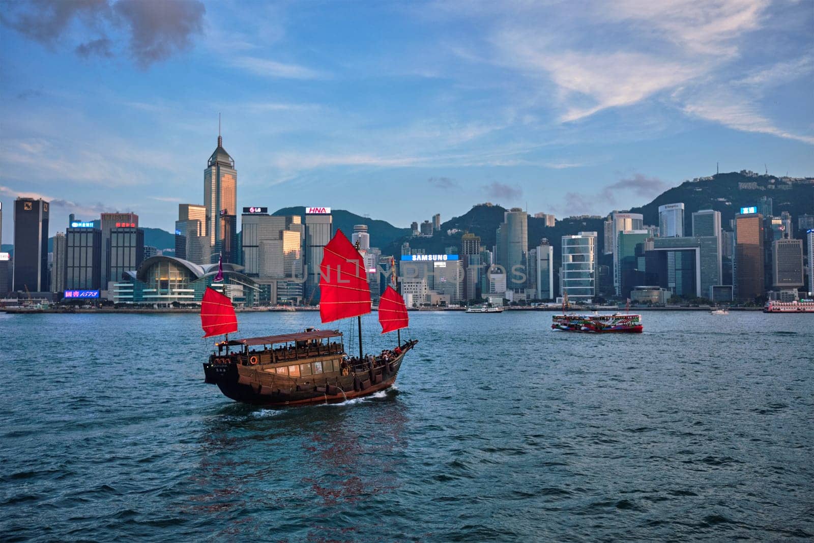 HONG KONG, CHINA - MAY 1, 2018: Hong Kong skyline cityscape downtown skyscrapers over Victoria Harbour in the evening with junk tourist ferry boat on sunset. Hong Kong, China