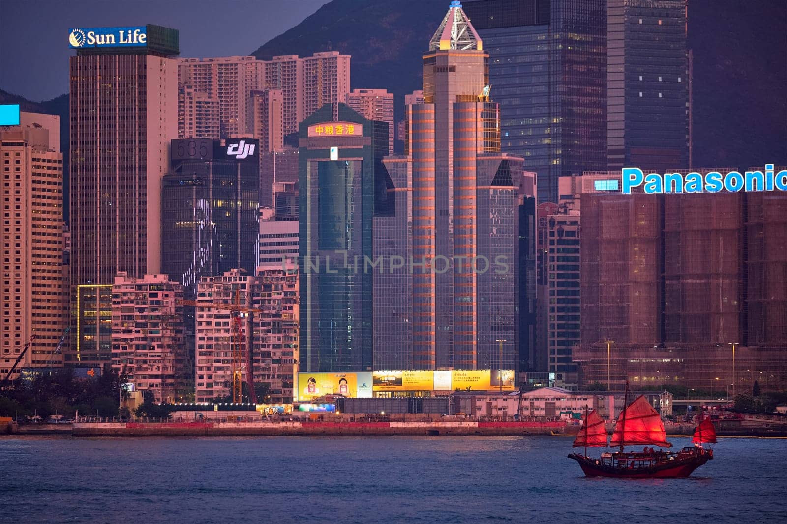 HONG KONG, CHINA - MAY 1, 2018: Tourist junk boat ferry with red sails and Hong Kong skyline cityscape downtown skyscrapers over Victoria Harbour in the evening. Hong Kong, China