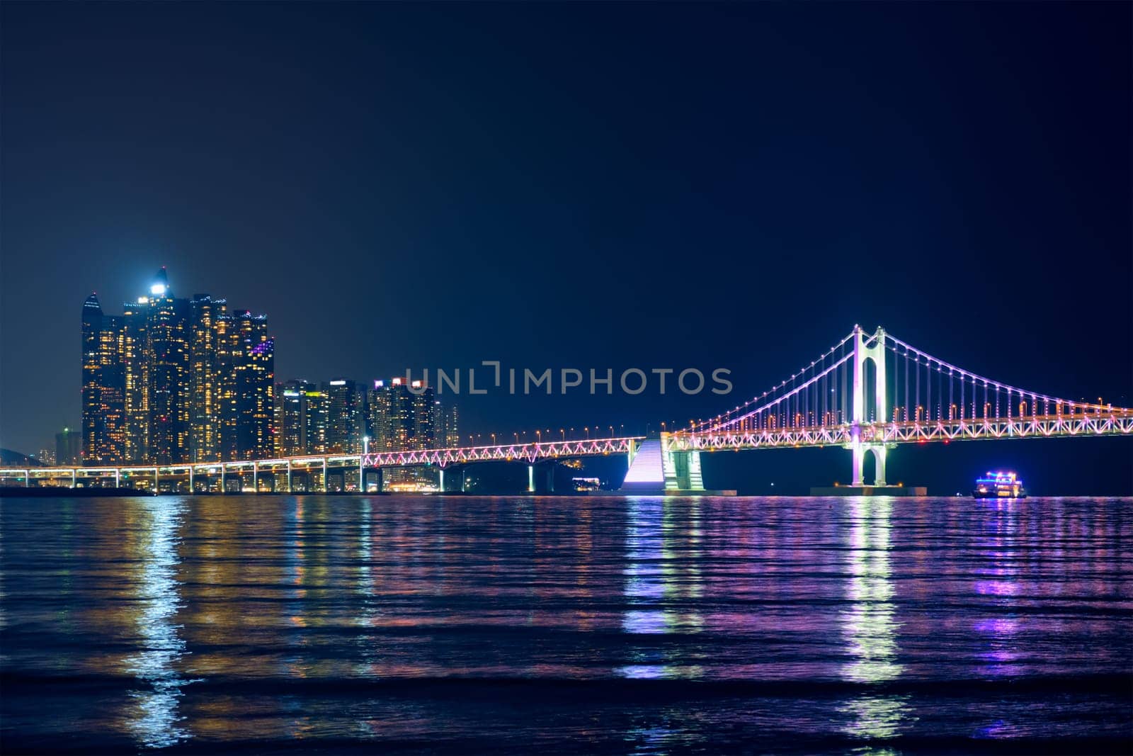 Gwangan Bridge and skyscrapers illuminated in the night and a ship. Busan, South Korea
