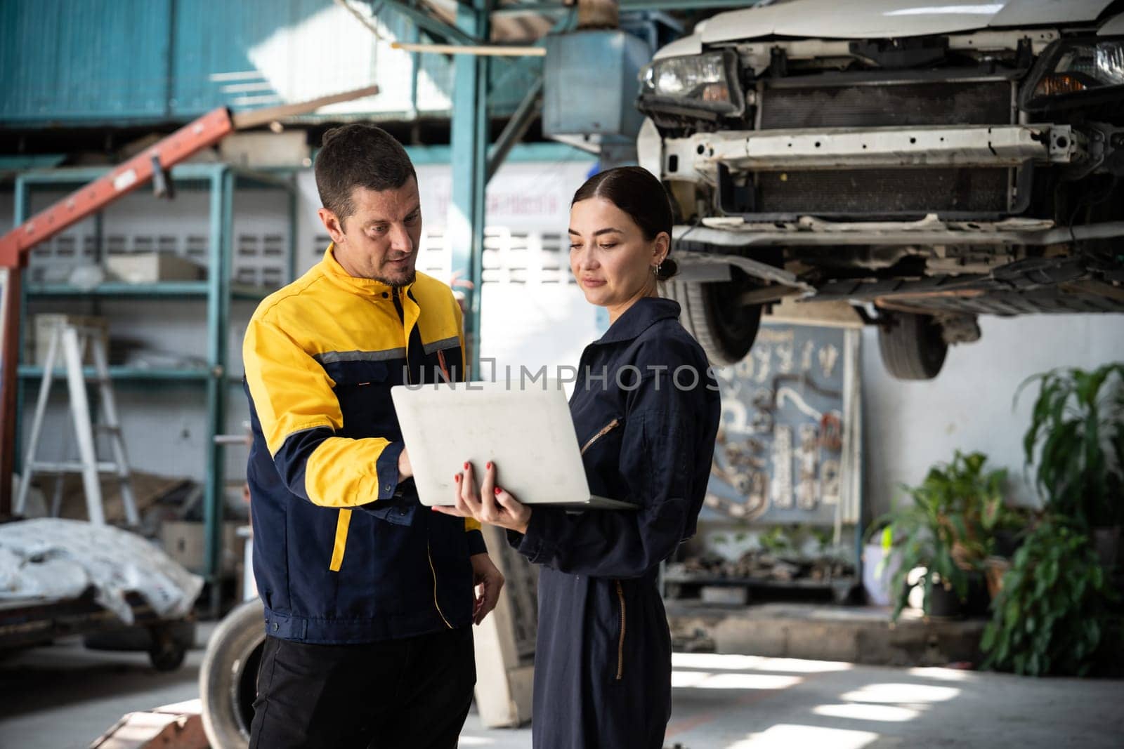 Two vehicle mechanic working together, conduct car inspection with laptop. Automotive service technician in uniform carefully make diagnostic troubleshooting to identify error. oxus