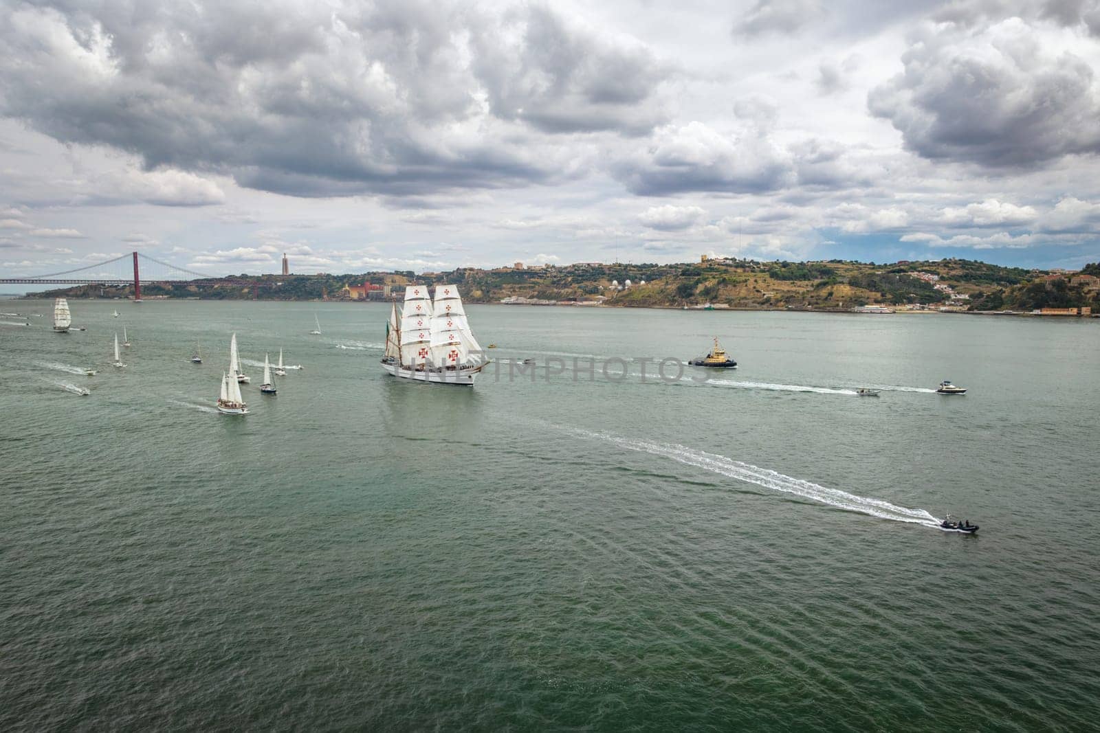 Aerial drone view of tall ships with sails sailing in Tagus river towards the Atlantic ocean in Lisbon, Portugal